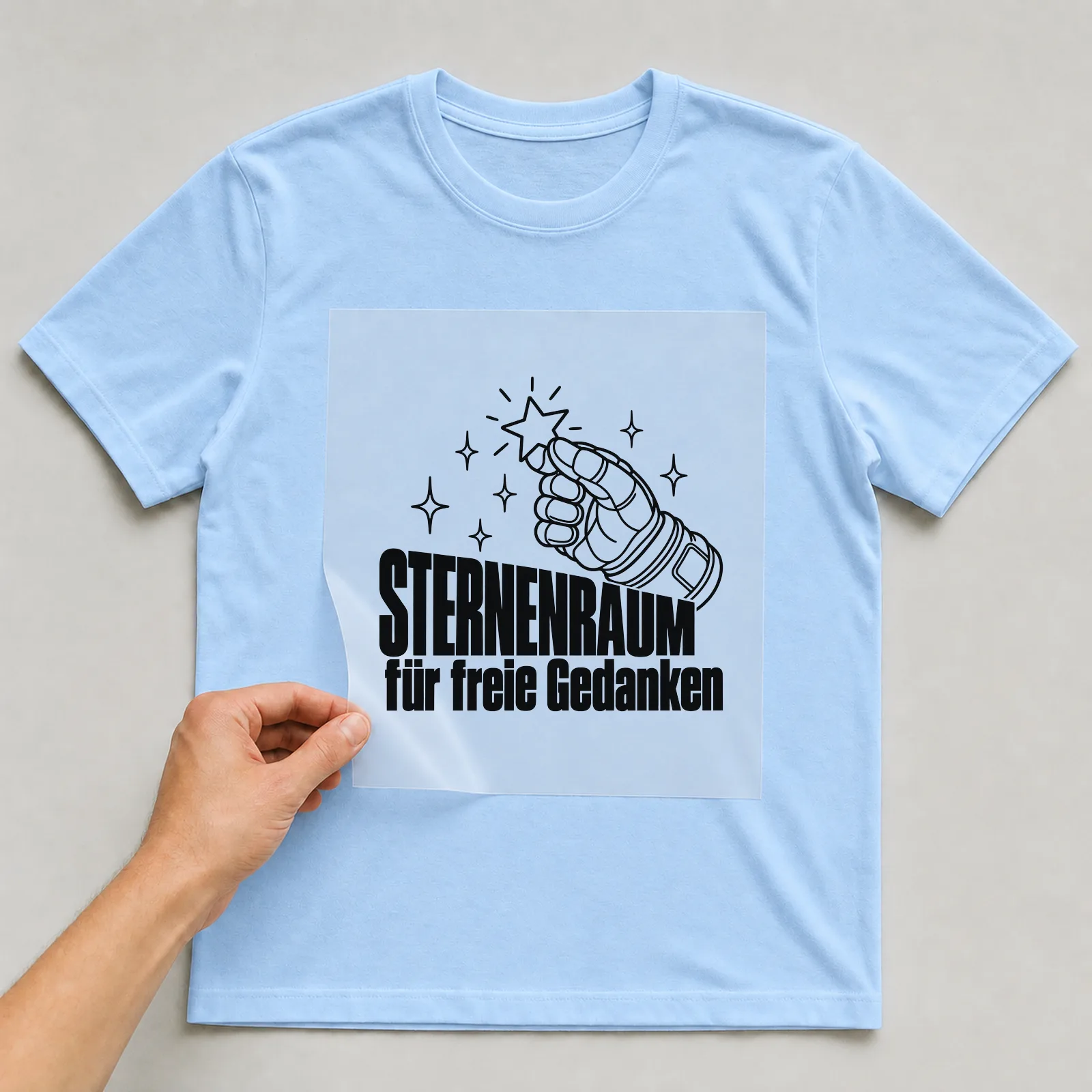Bügelbild „Sternenraum für freie Gedanken“ auf hellblauem T-Shirt, Folie wird aufgelegt