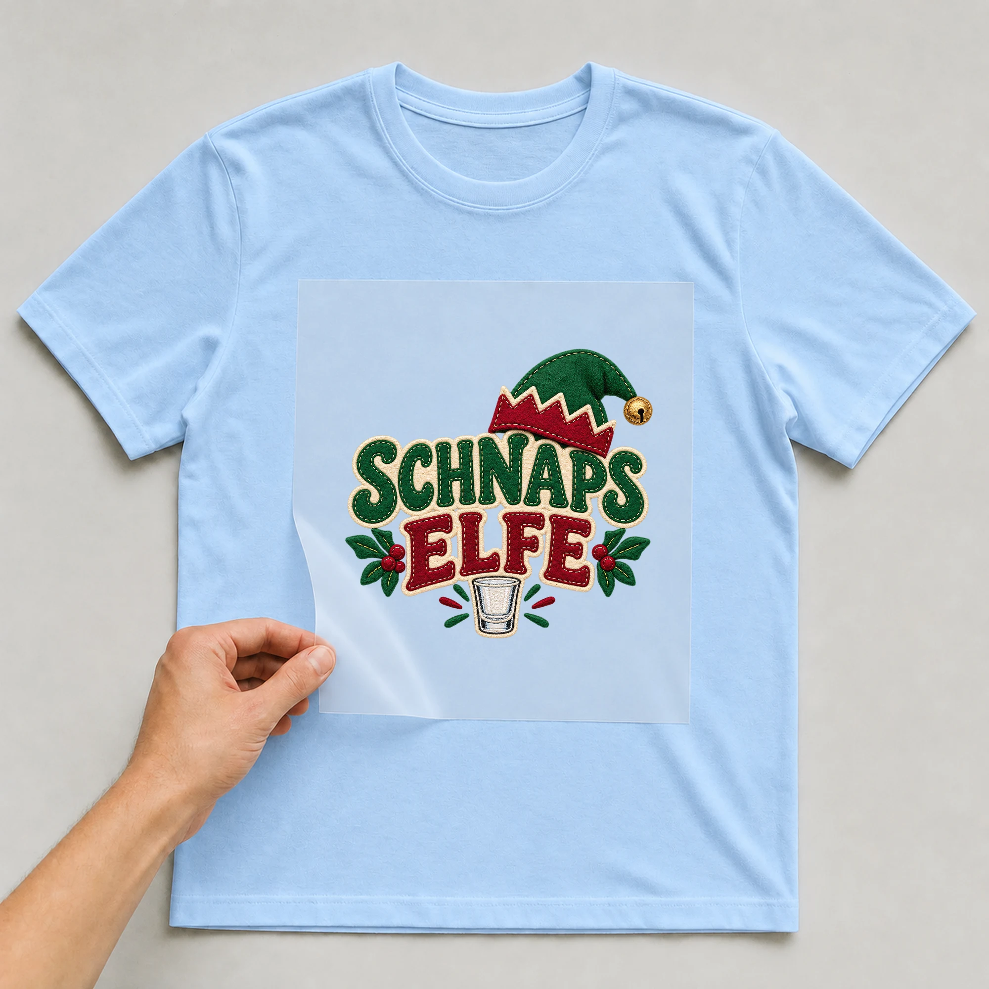 Bügelbild „Schnaps Elfe“ auf babyblauem T-Shirt, Folie wird aufgelegt