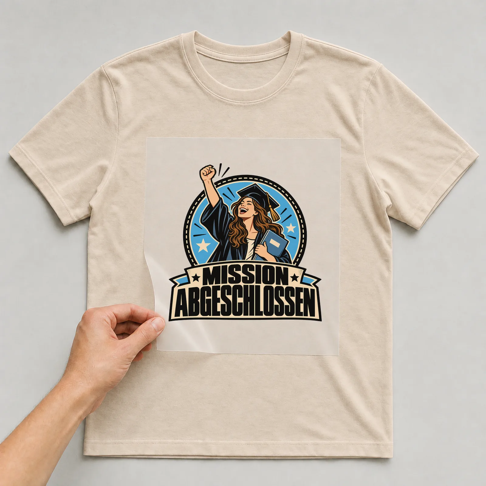 Bügelbild „Mission abgeschlossen“ auf beigem T-Shirt, Folie wird aufgelegt