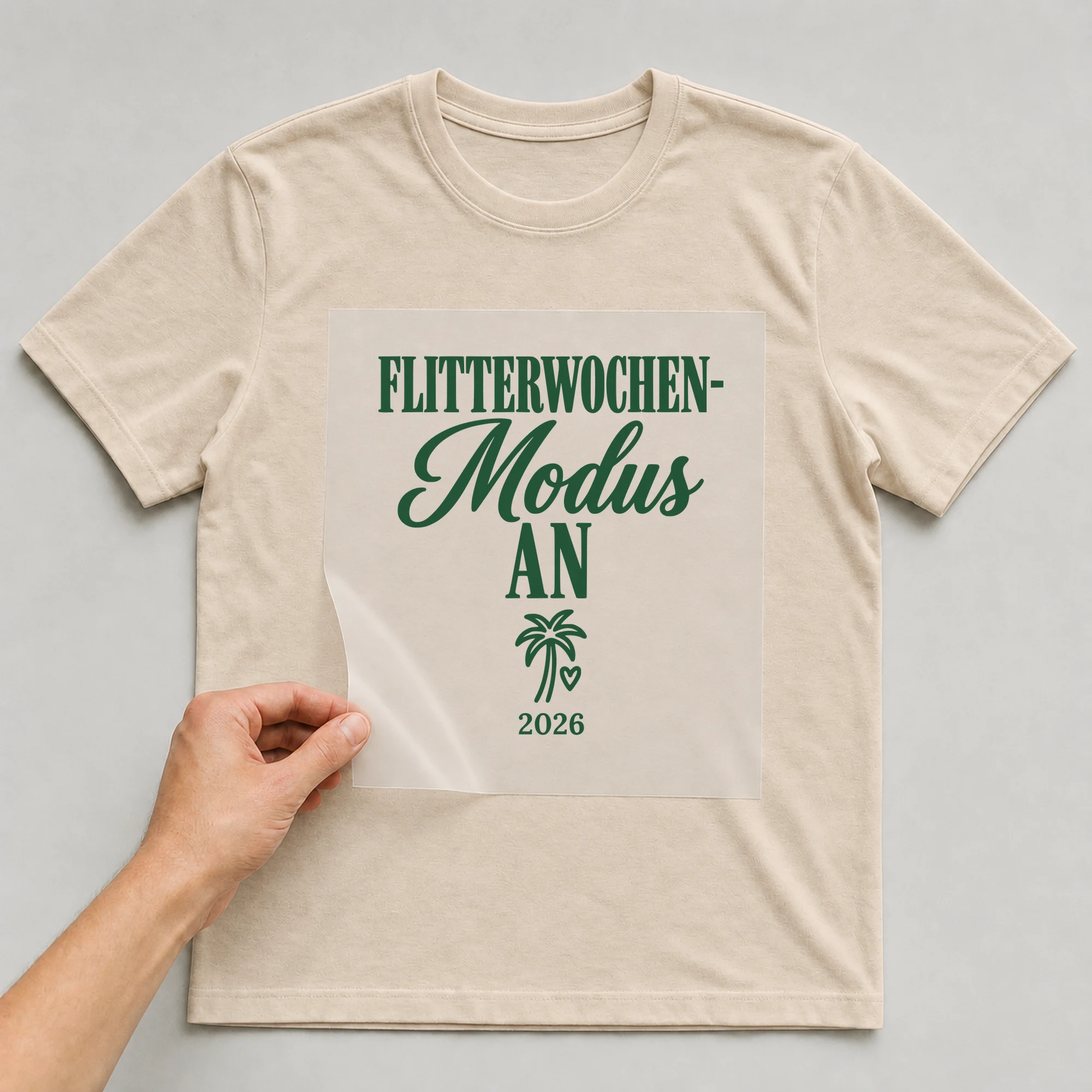 Bügelbild Flitterwochen-Modus an mit Jahr auf beigem T-Shirt, Folie wird aufgelegt