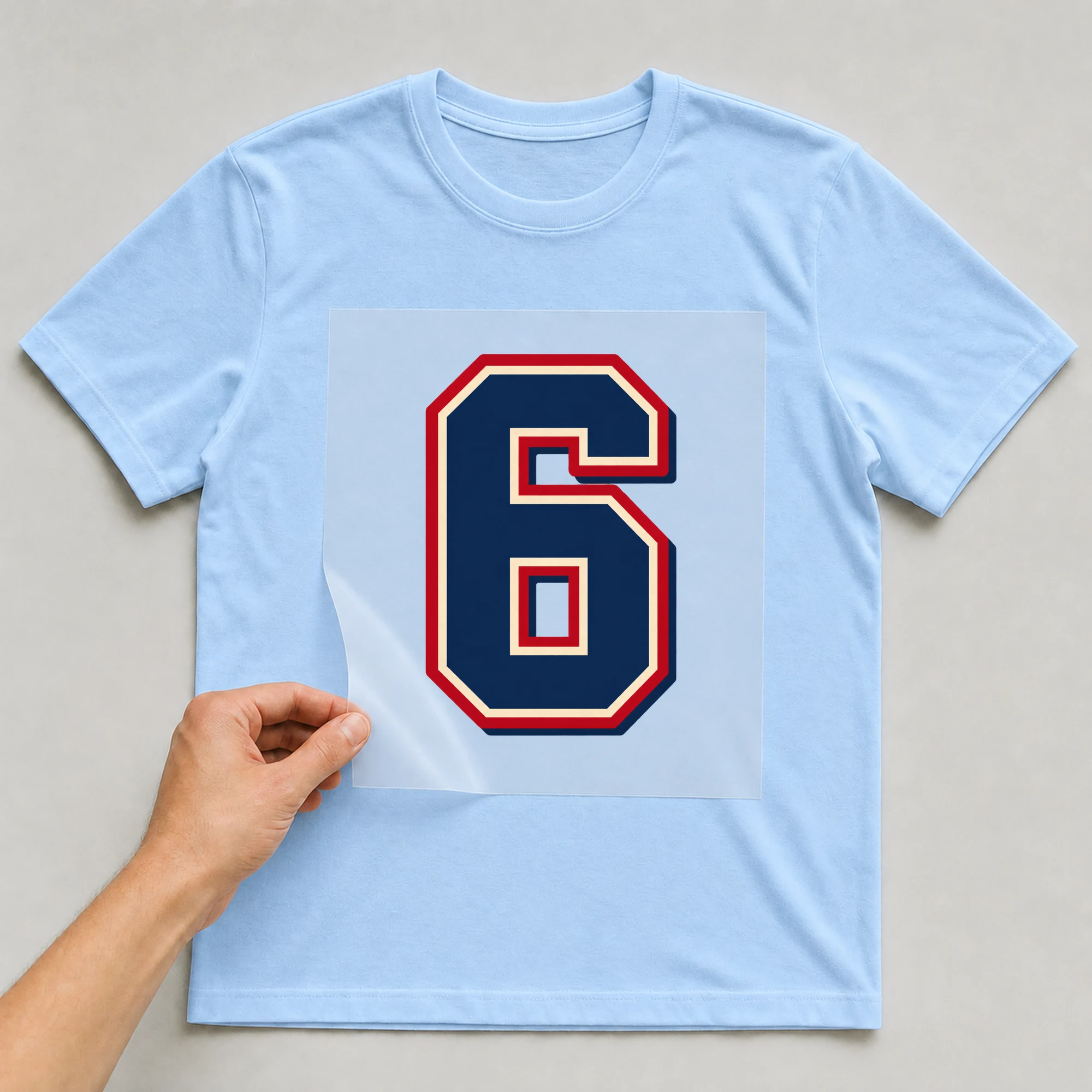 Bügelbild „Zahl 6 im Retro-College-Stil“ auf babyblauem T-Shirt, Folie wird aufgelegt