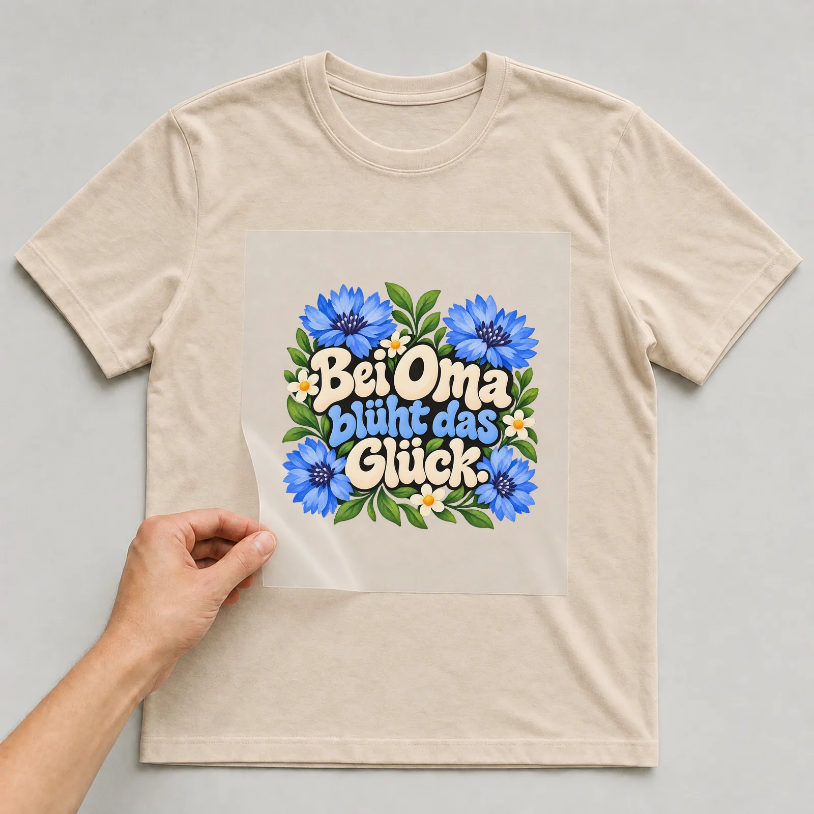 Bügelbild „Bei Oma blüht das Glück“ auf beigem T-Shirt, Folie wird aufgelegt