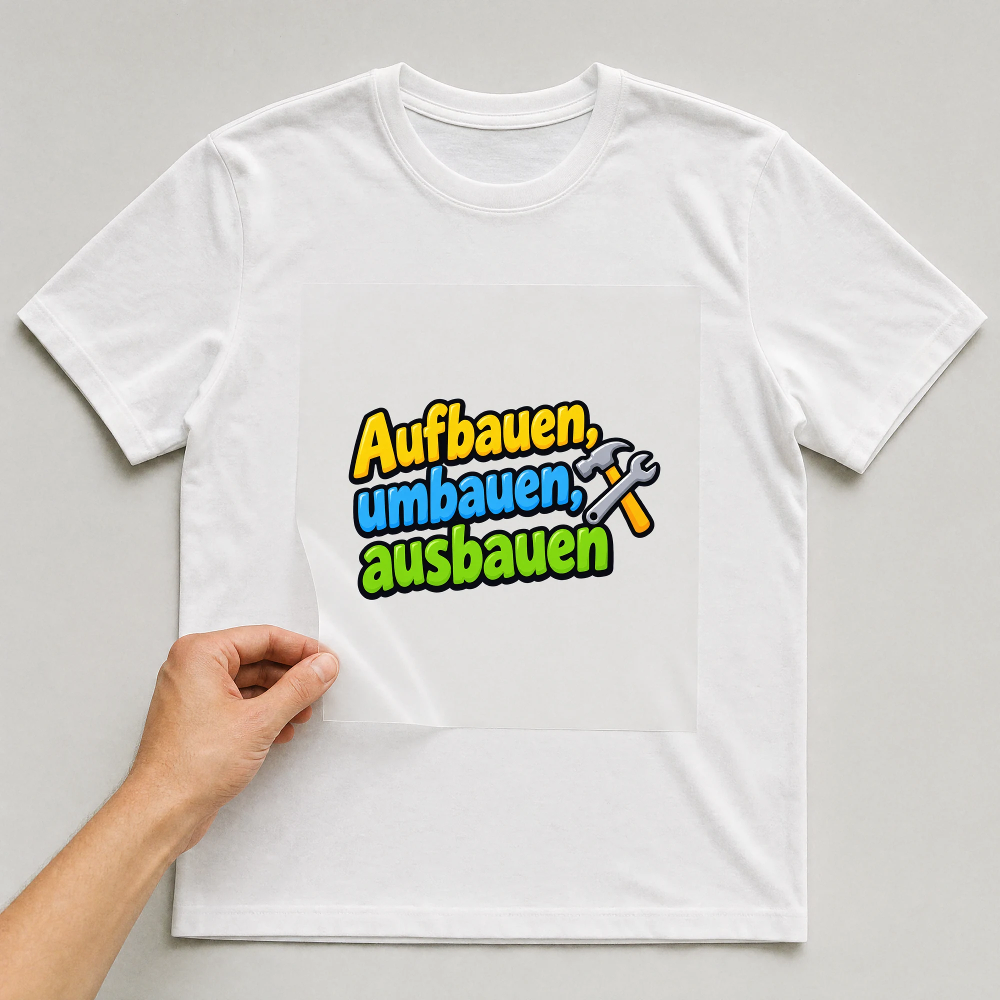 Bügelbild „Aufbauen, umbauen, ausbauen“ auf weißem T-Shirt, Folie wird aufgelegt