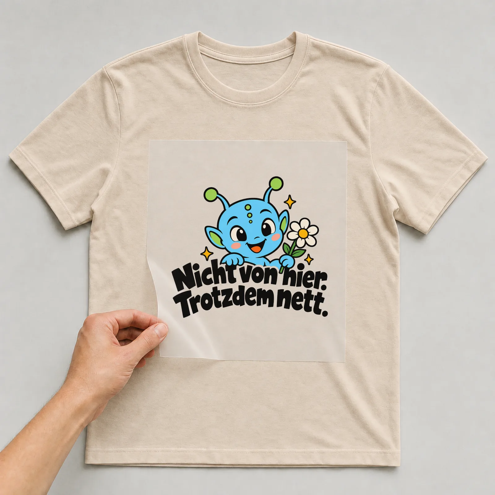 Bügelbild „Nicht von hier. Trotzdem nett.“ auf beigem T-Shirt, Folie wird aufgelegt