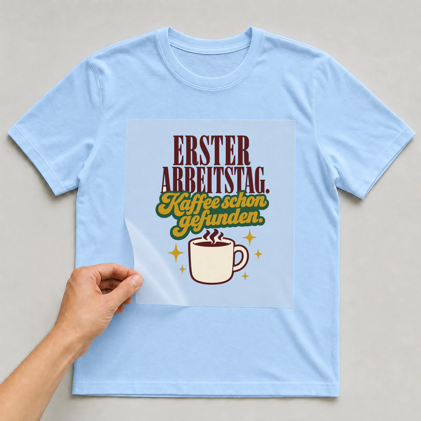 Bügelbild Erster Arbeitstag. Kaffee schon gefunden. auf hellblauem T-Shirt, Folie wird aufgelegt