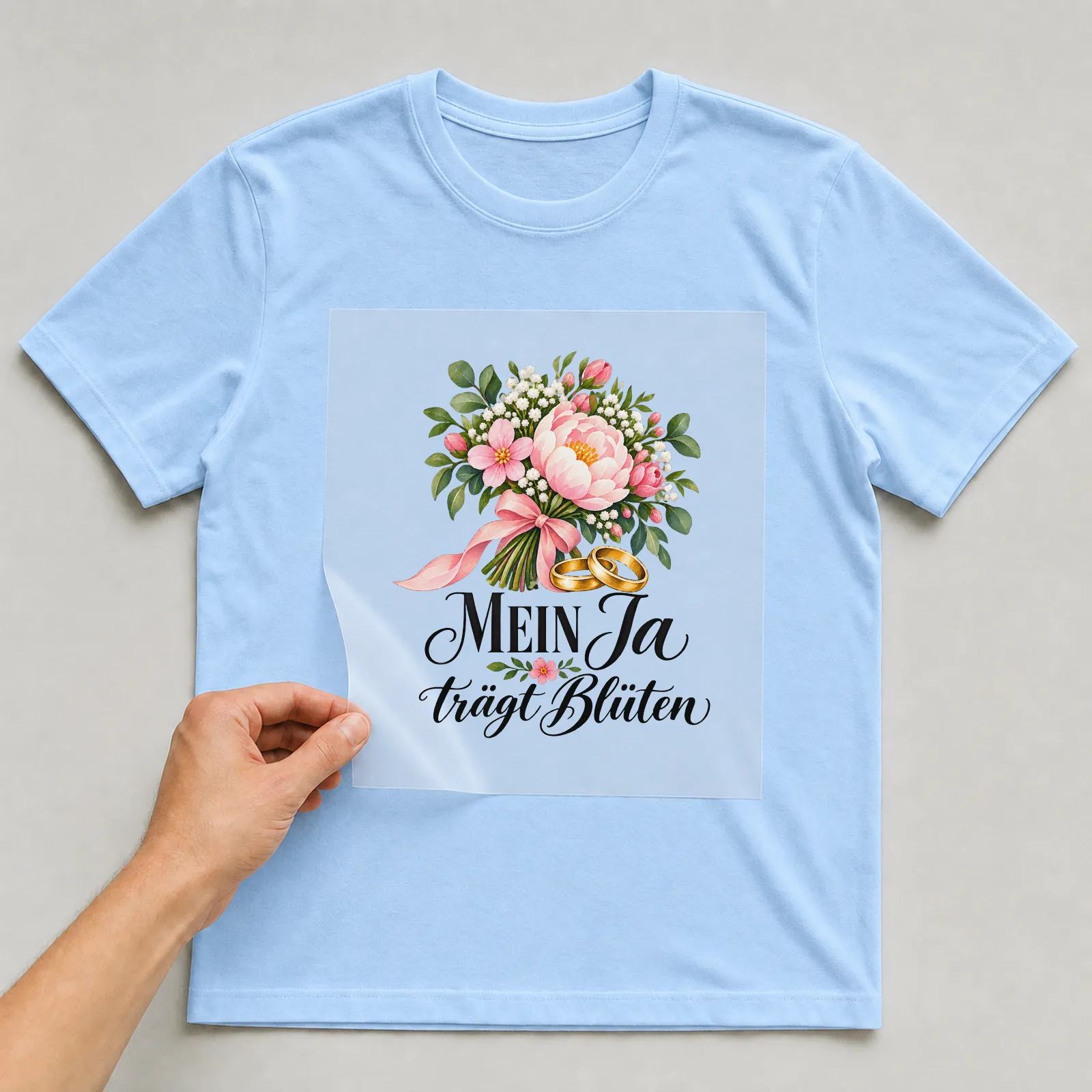 Bügelbild „Mein Ja trägt Blüten“ auf hellblauem T-Shirt, Folie wird aufgelegt