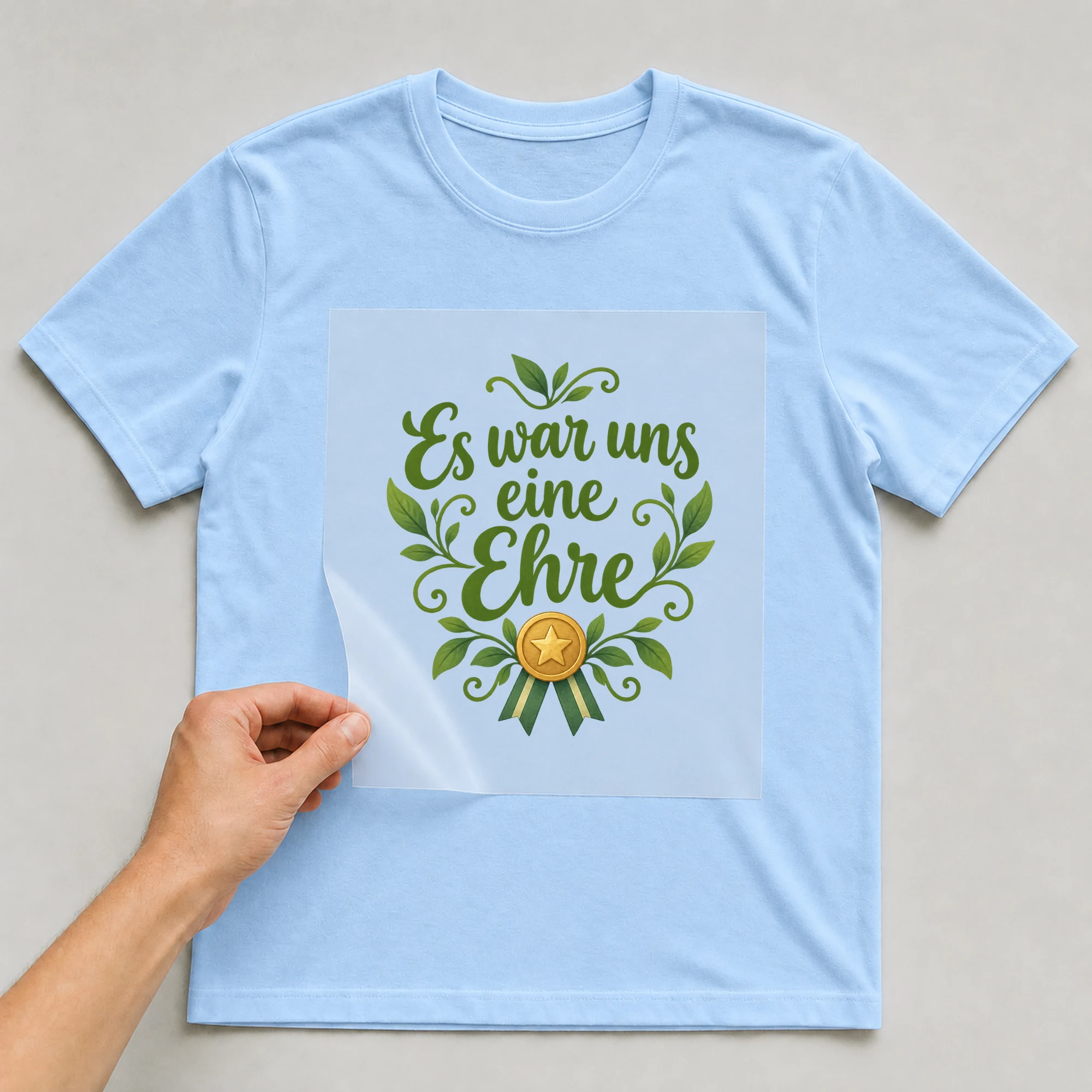 Bügelbild „Es war uns eine Ehre“ auf babyblauem T-Shirt, Folie wird aufgelegt