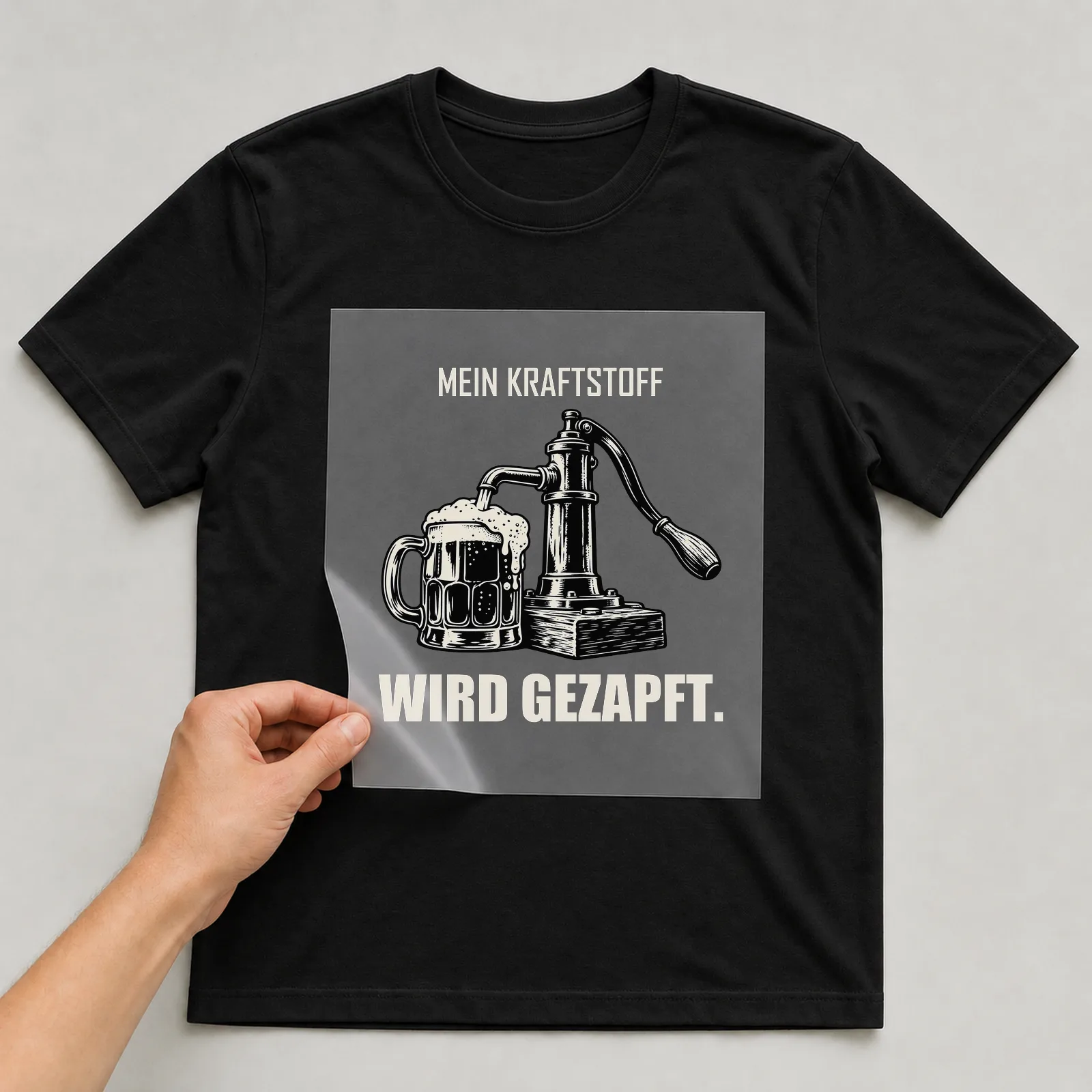 Bügelbild „Mein Kraftstoff wird gezapft“ auf schwarzem T-Shirt, Folie wird aufgelegt