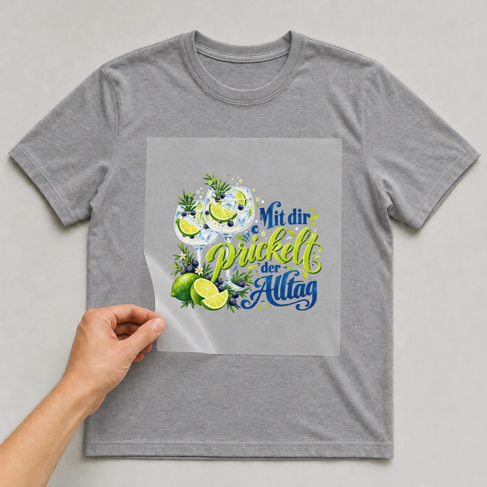 Bügelbild „Mit dir prickelt der Alltag“ auf grauem T-Shirt, Folie wird aufgelegt