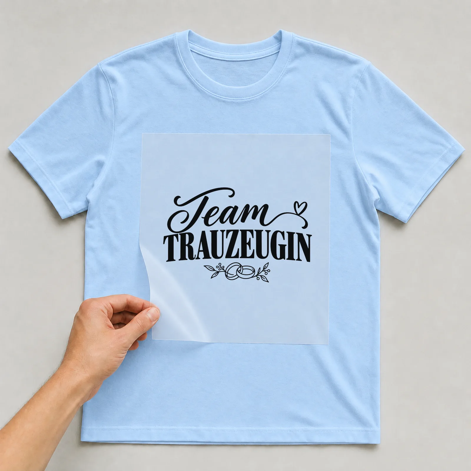 Bügelbild „Team Trauzeugin“ auf hellblauem T-Shirt, Folie wird aufgelegt