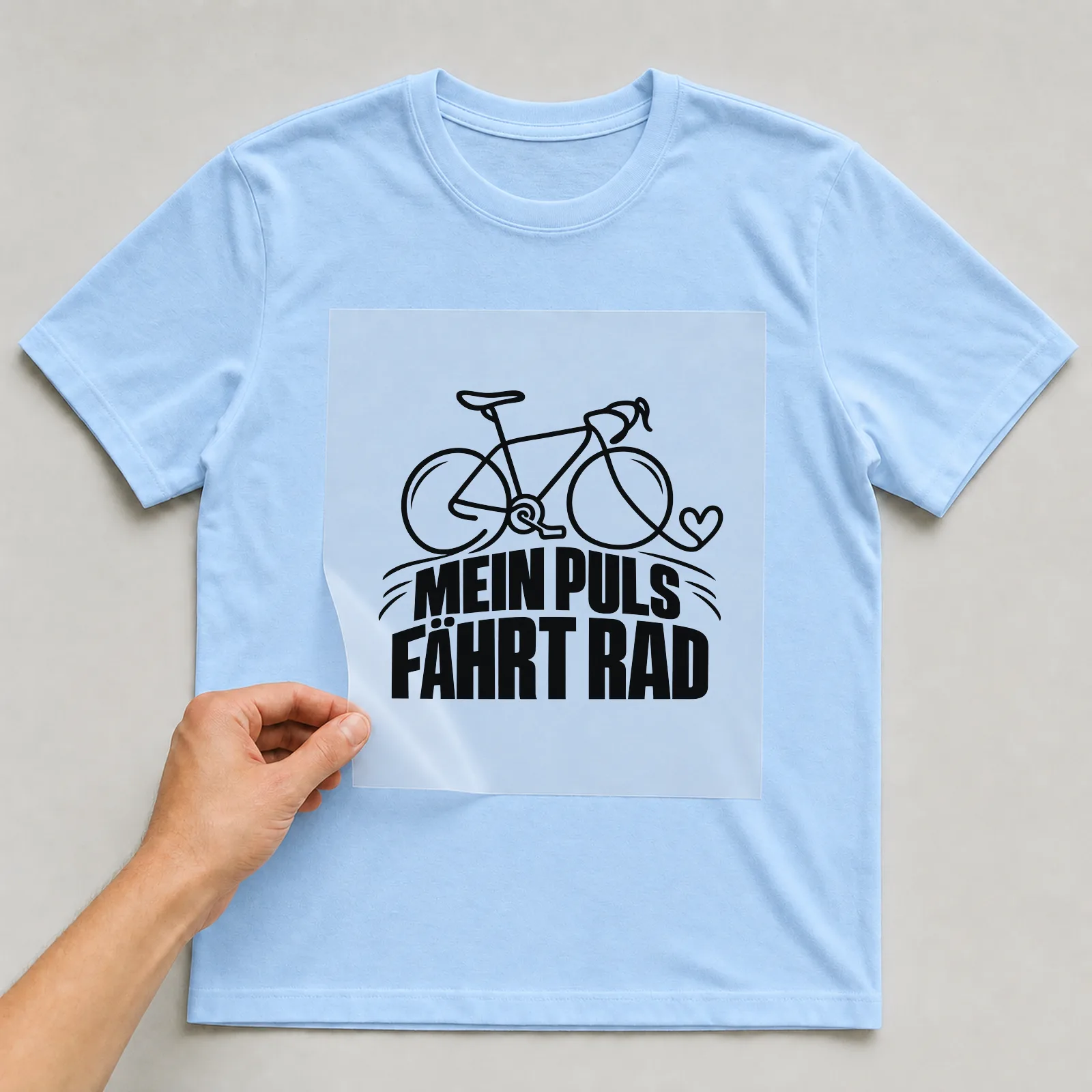 Bügelbild „Mein Puls fährt Rad“ auf hellblauem T-Shirt, Folie wird aufgelegt