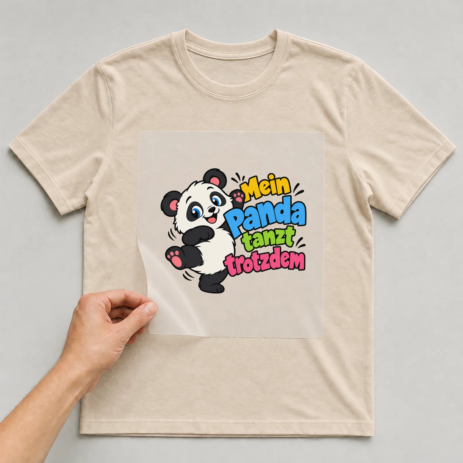 Bügelbild „Mein Panda tanzt trotzdem“ auf beigem T-Shirt, Folie wird aufgelegt