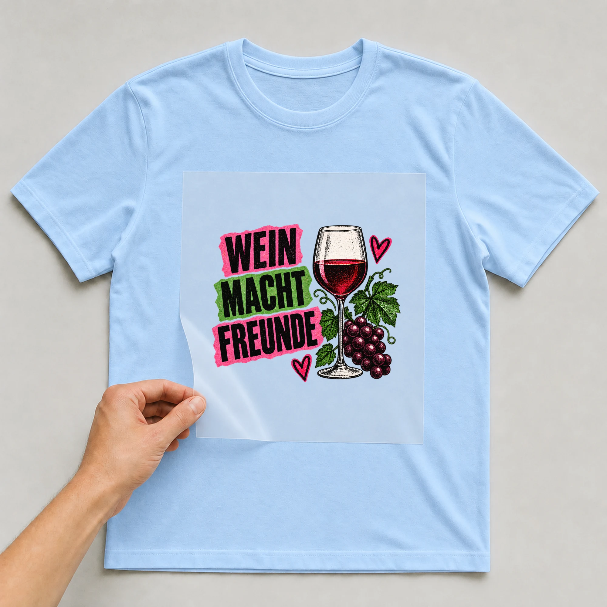 Bügelbild „Wein macht Freunde“ auf hellblauem T-Shirt, Folie wird aufgelegt