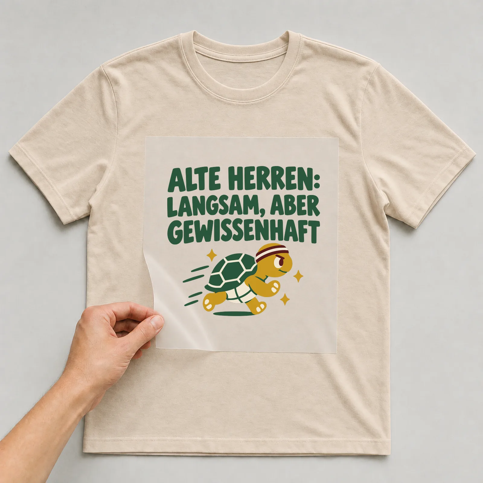 Bügelbild Alte Herren: langsam, aber gewissenhaft auf beigem T-Shirt, Folie wird aufgelegt