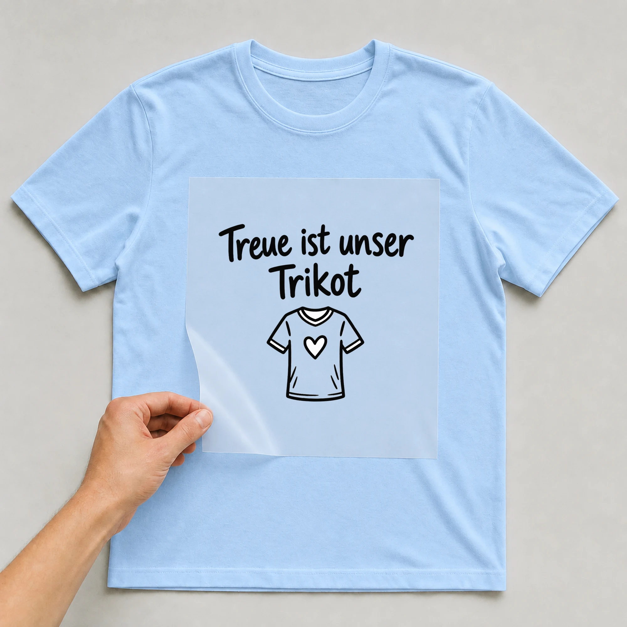 Bügelbild „Treue ist unser Trikot“ auf babyblauem T-Shirt, Folie wird aufgelegt