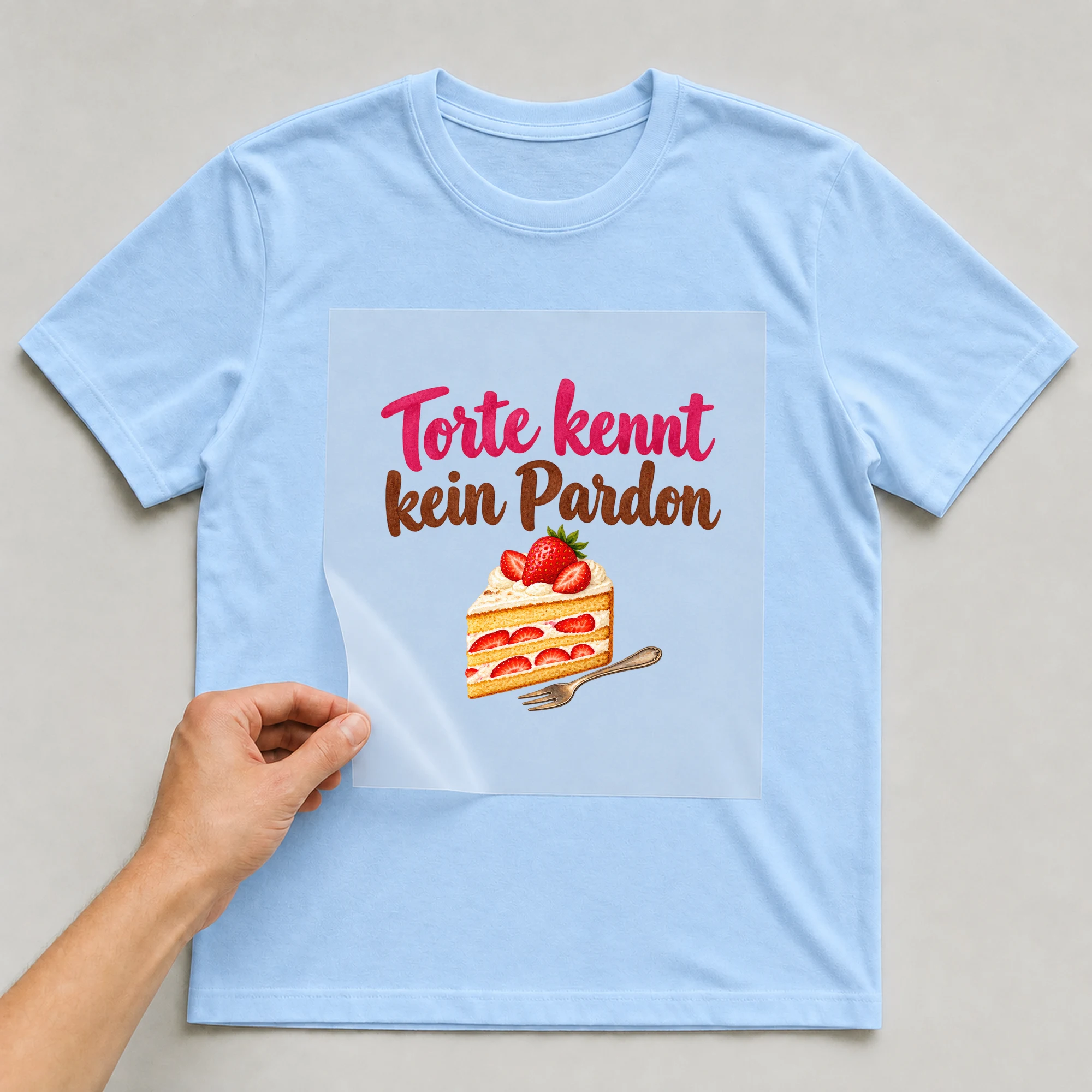 Bügelbild „Torte kennt kein Pardon“ auf babyblauem T-Shirt, Folie wird aufgelegt