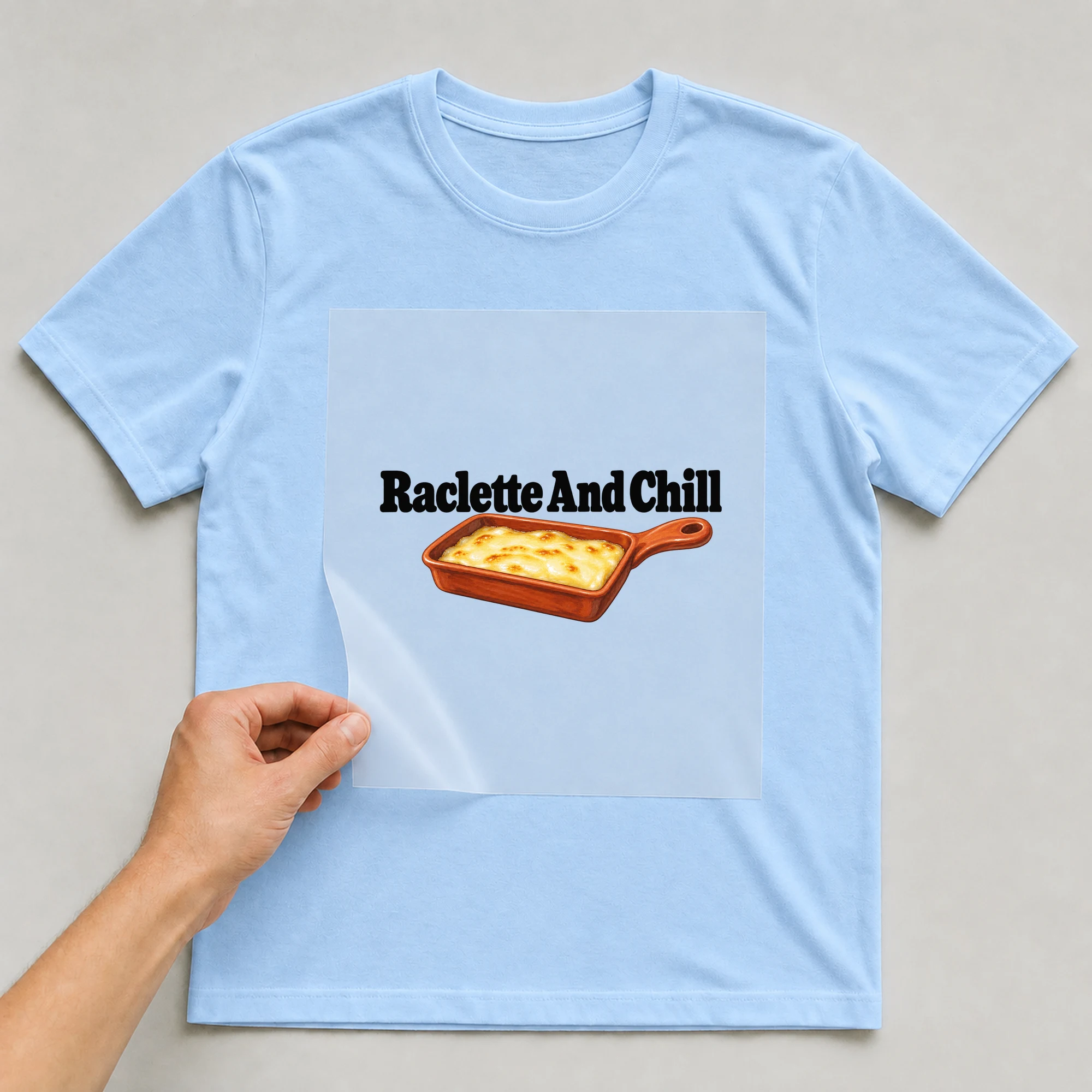 Bügelbild „Raclette And Chill“ auf babyblauem T-Shirt, Folie wird aufgelegt