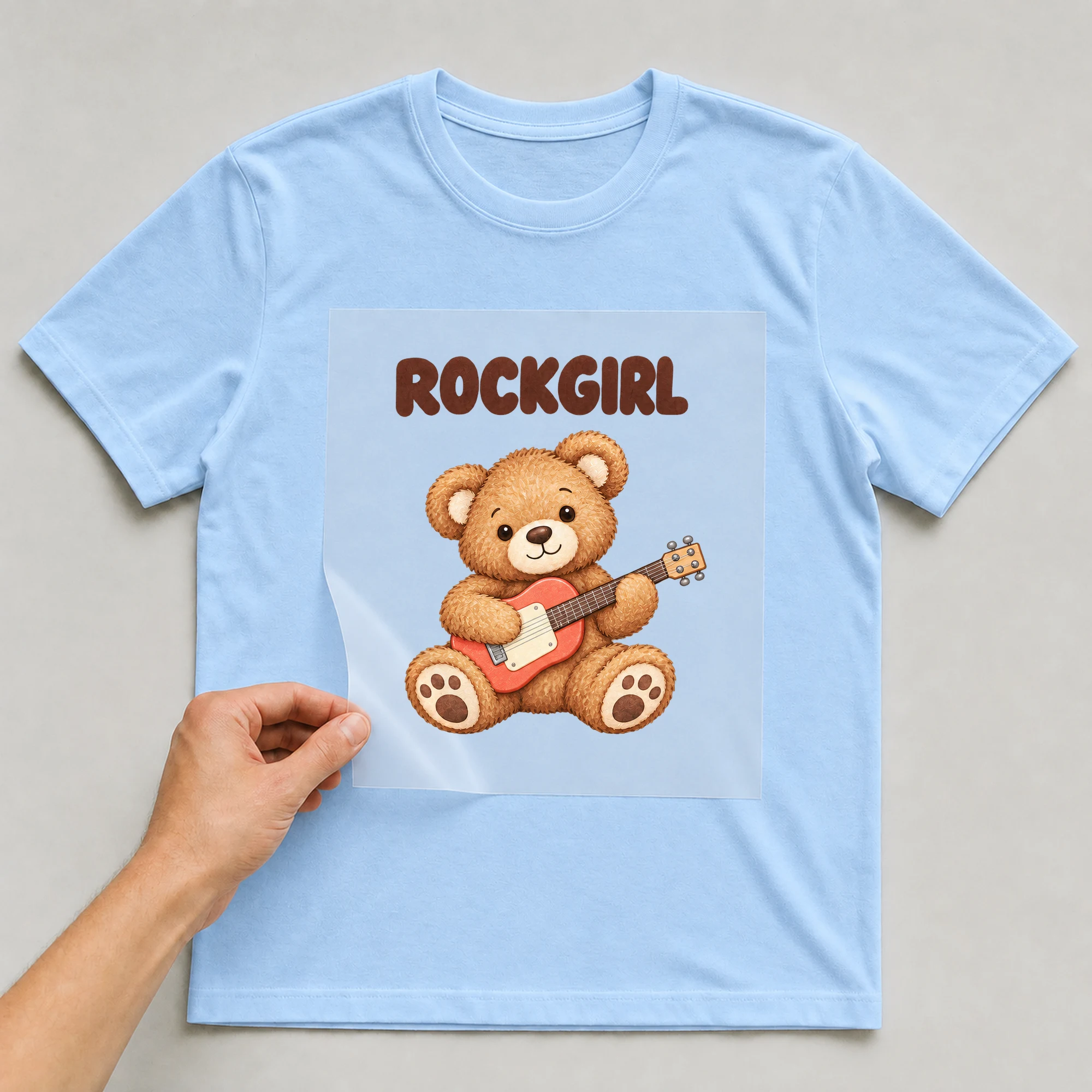 Bügelbild „ROCKGIRL“ auf babyblauem T-Shirt, Folie wird aufgelegt