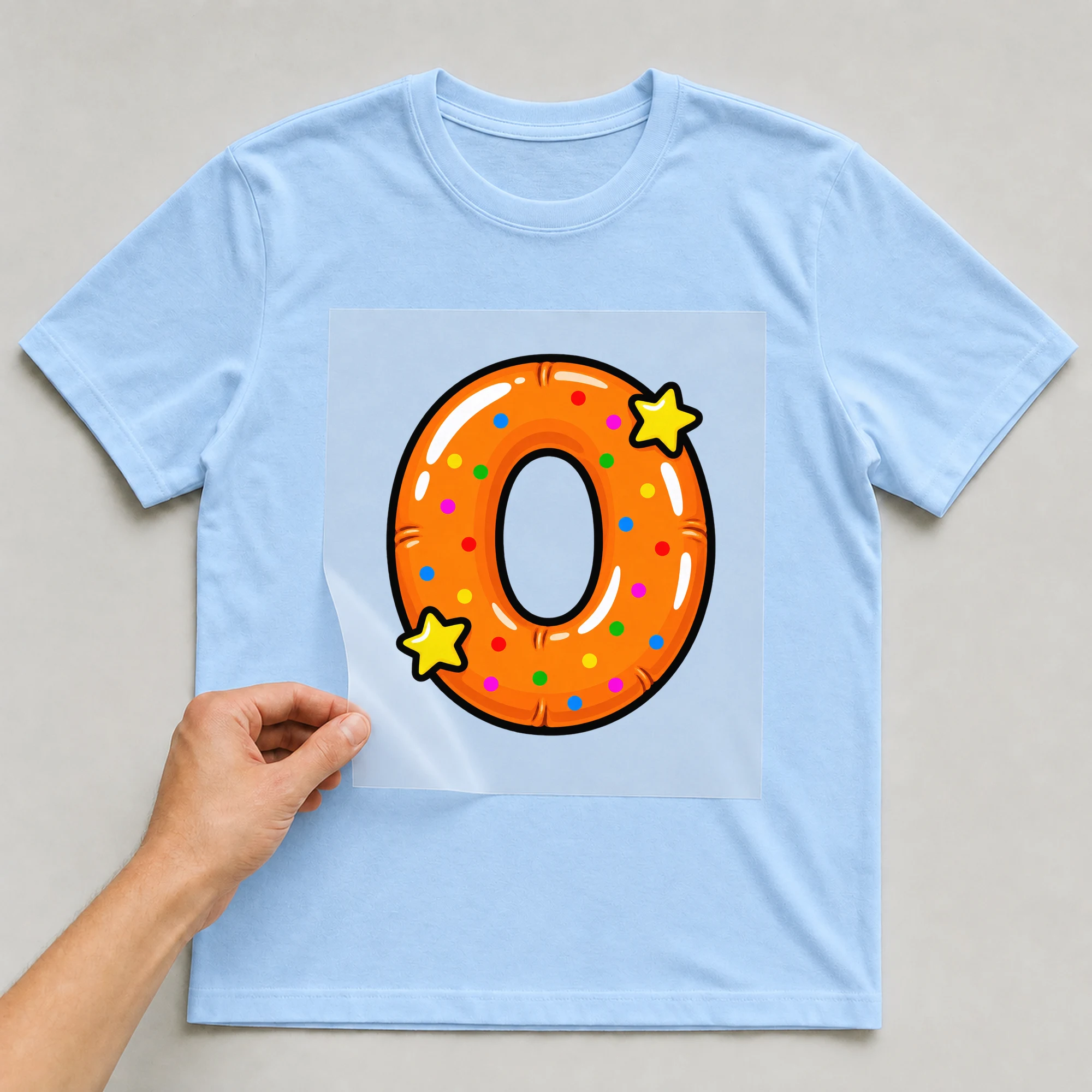 Bügelbild „Buchstabe O im Comic-Ballon-Stil“ auf babyblauem T-Shirt, Folie wird aufgelegt