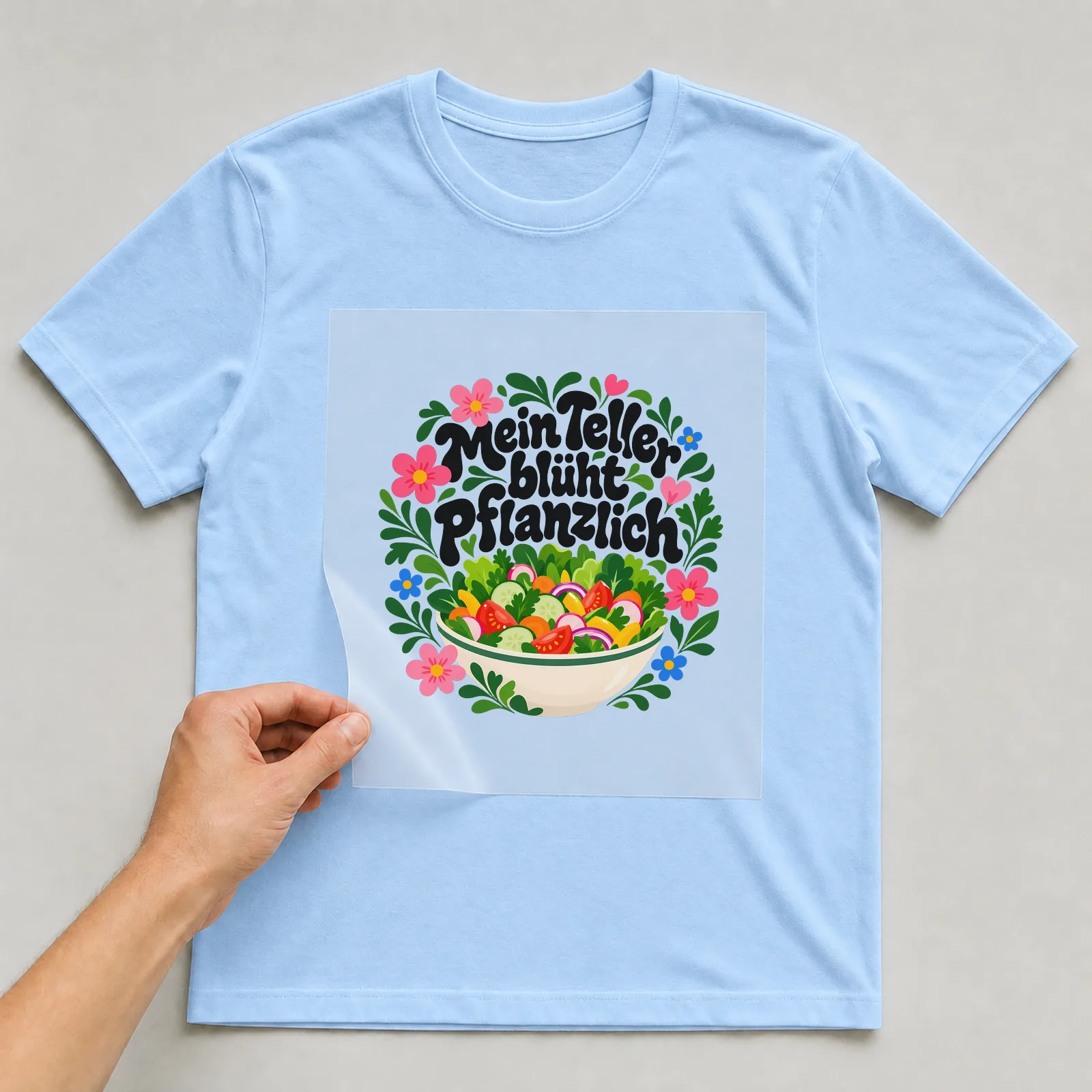 Bügelbild „Mein Teller blüht pflanzlich“ auf hellblauem T-Shirt, Folie wird aufgelegt