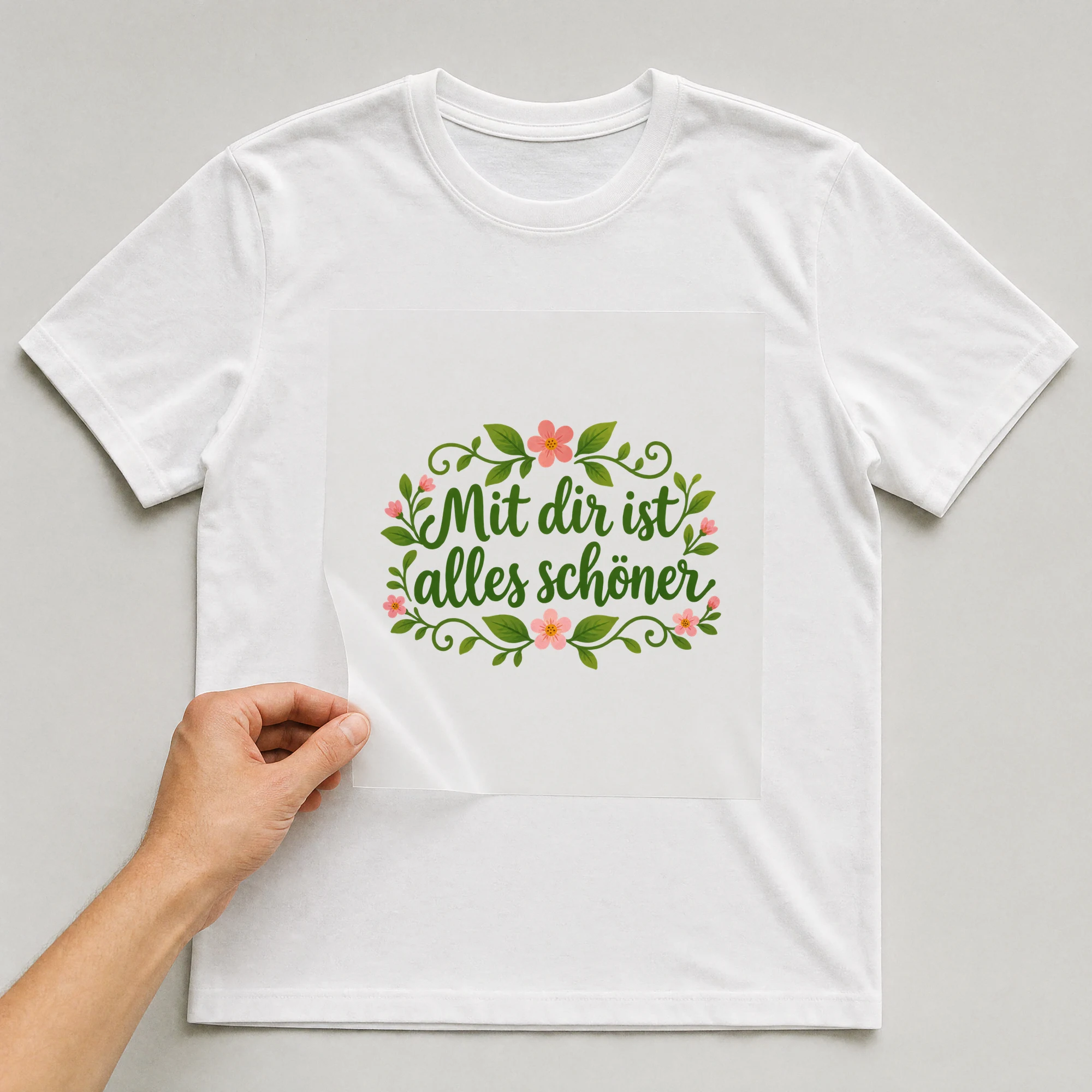 Bügelbild „Mit dir ist alles schöner“ auf weißem T-Shirt, Folie wird aufgelegt