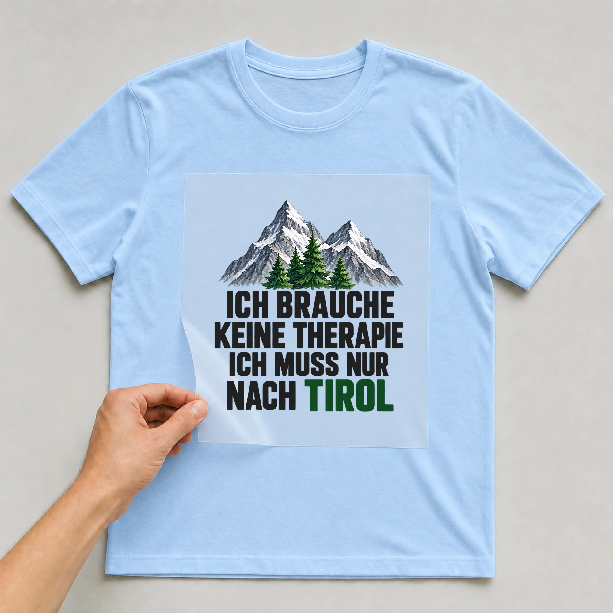 Bügelbild „Ich brauche keine Therapie ich muss nur nach Tirol“ auf babyblauem T-Shirt, Folie wird aufgelegt