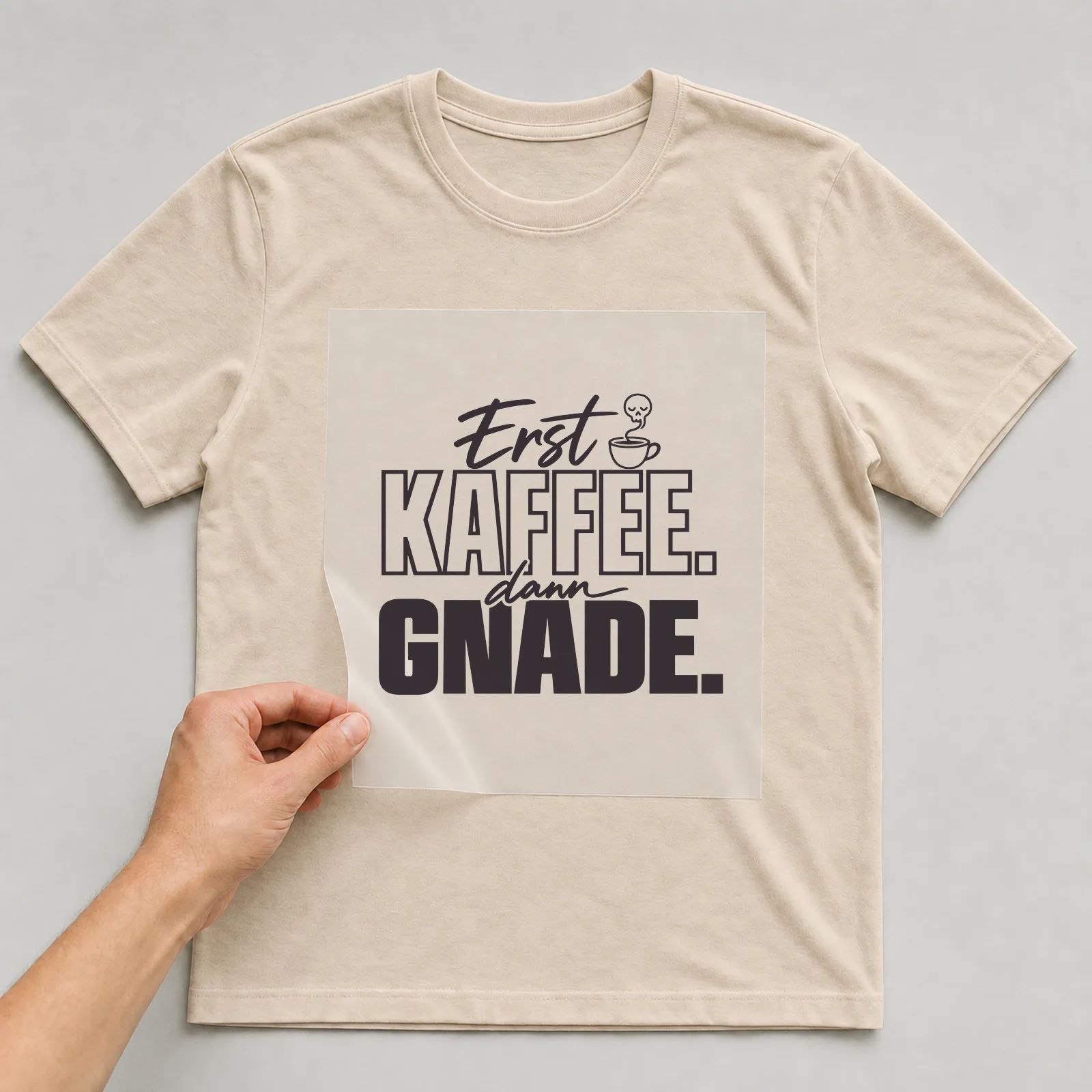 Bügelbild „Erst Kaffee. Dann Gnade.“ (Schrift Konturen, Nr. 2) auf beigem T-Shirt, Folie wird aufgelegt
