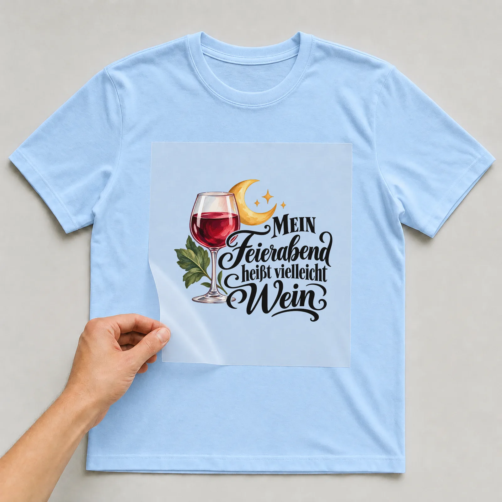 Bügelbild „MEIN Feierabend heißt vielleicht Wein“ auf hellblauem T-Shirt, Folie wird aufgelegt