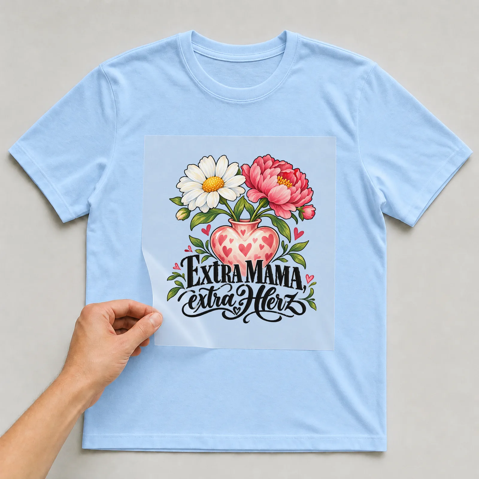 Bügelbild „Extra Mama, extra Herz“ auf hellblauem T-Shirt, Folie wird aufgelegt