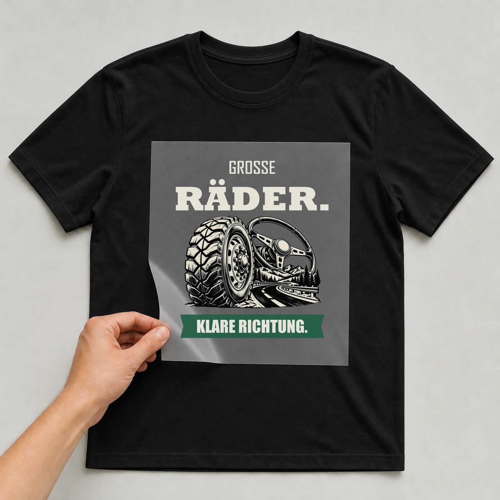 Bügelbild „Große Räder. Klare Richtung.“ auf schwarzem T-Shirt, Folie wird aufgelegt