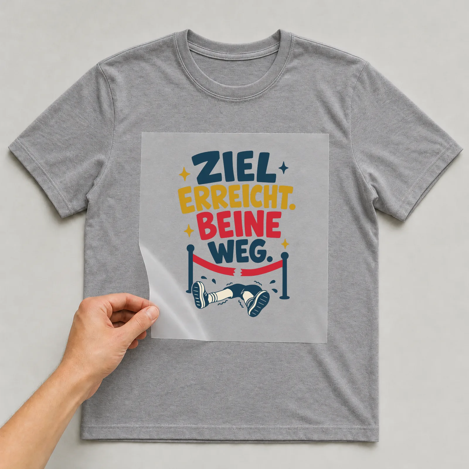 Bügelbild Ziel erreicht. Beine weg. auf grauem T-Shirt, Folie wird aufgelegt