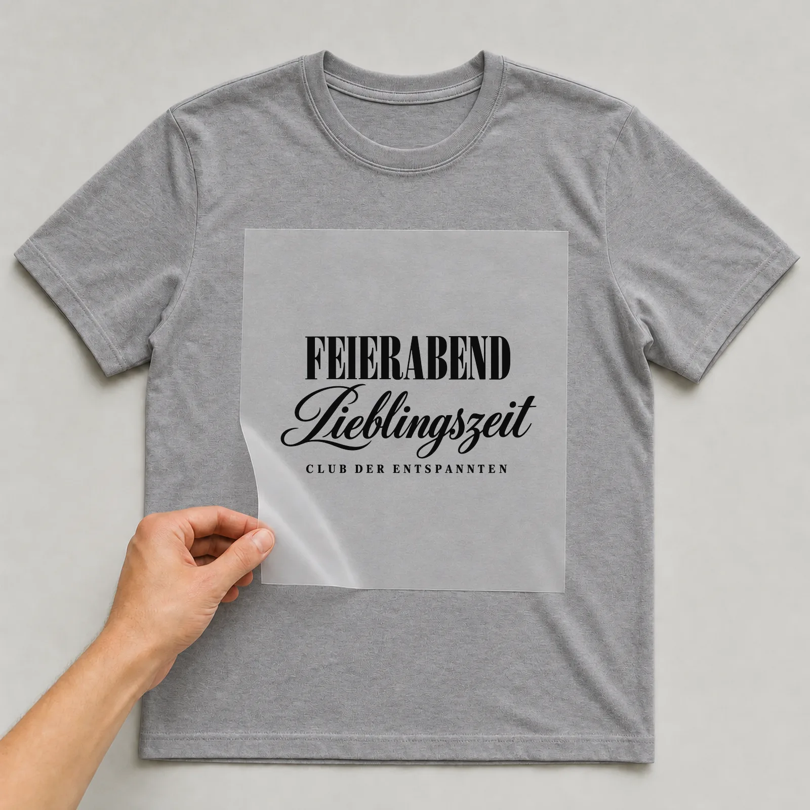 Bügelbild „FEIERABEND · Lieblingszeit · CLUB DER ENTSPANNTEN“ auf grauem T-Shirt, Folie wird aufgelegt