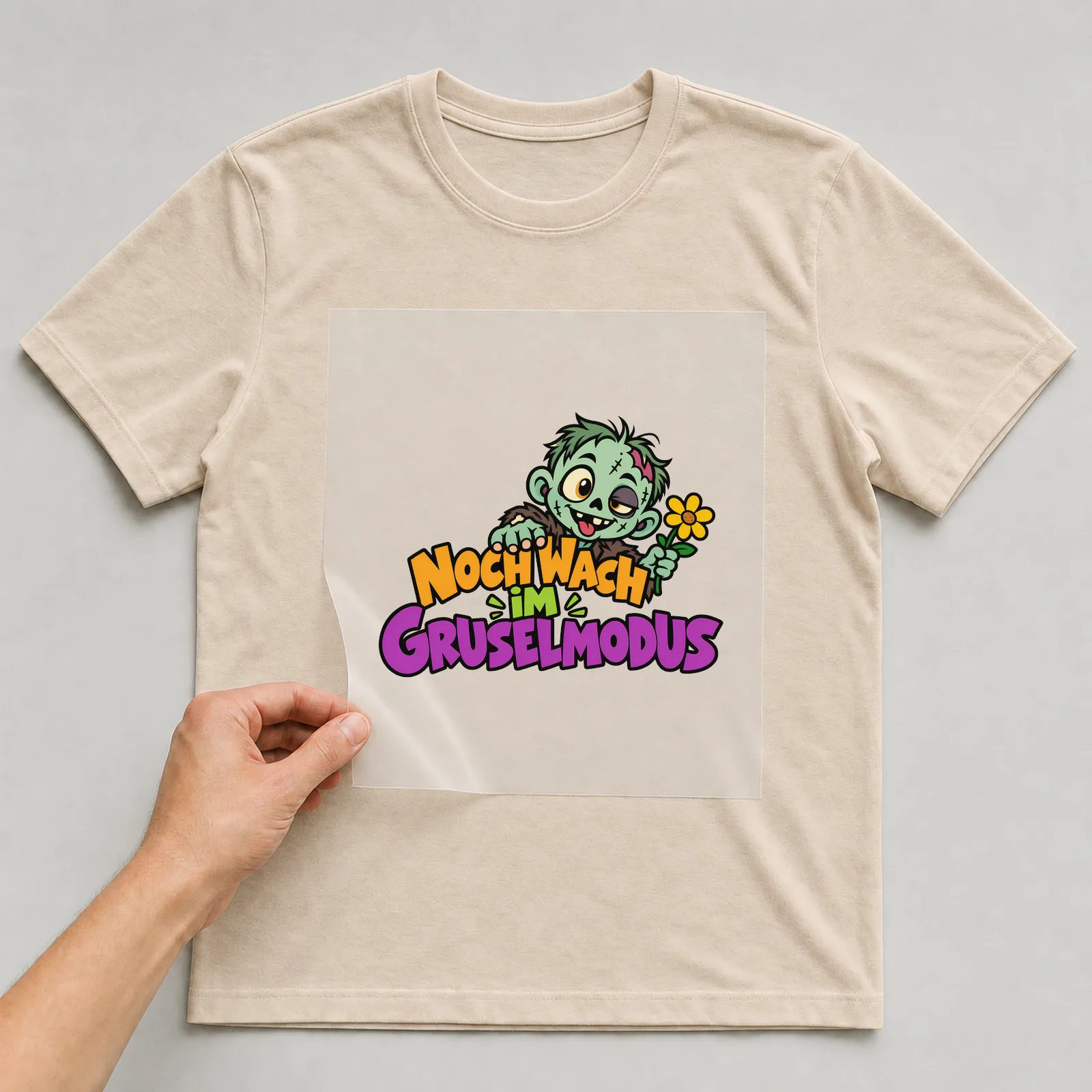 Bügelbild „Noch wach im Gruselmodus“ auf beigem T-Shirt, Folie wird aufgelegt