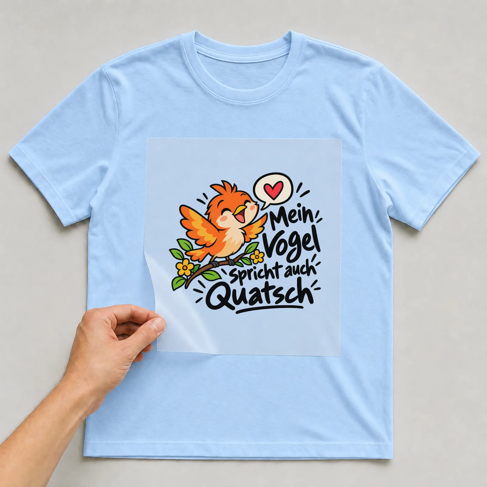 Bügelbild „Mein Vogel spricht auch Quatsch“ auf hellblauem T-Shirt, Folie wird aufgelegt