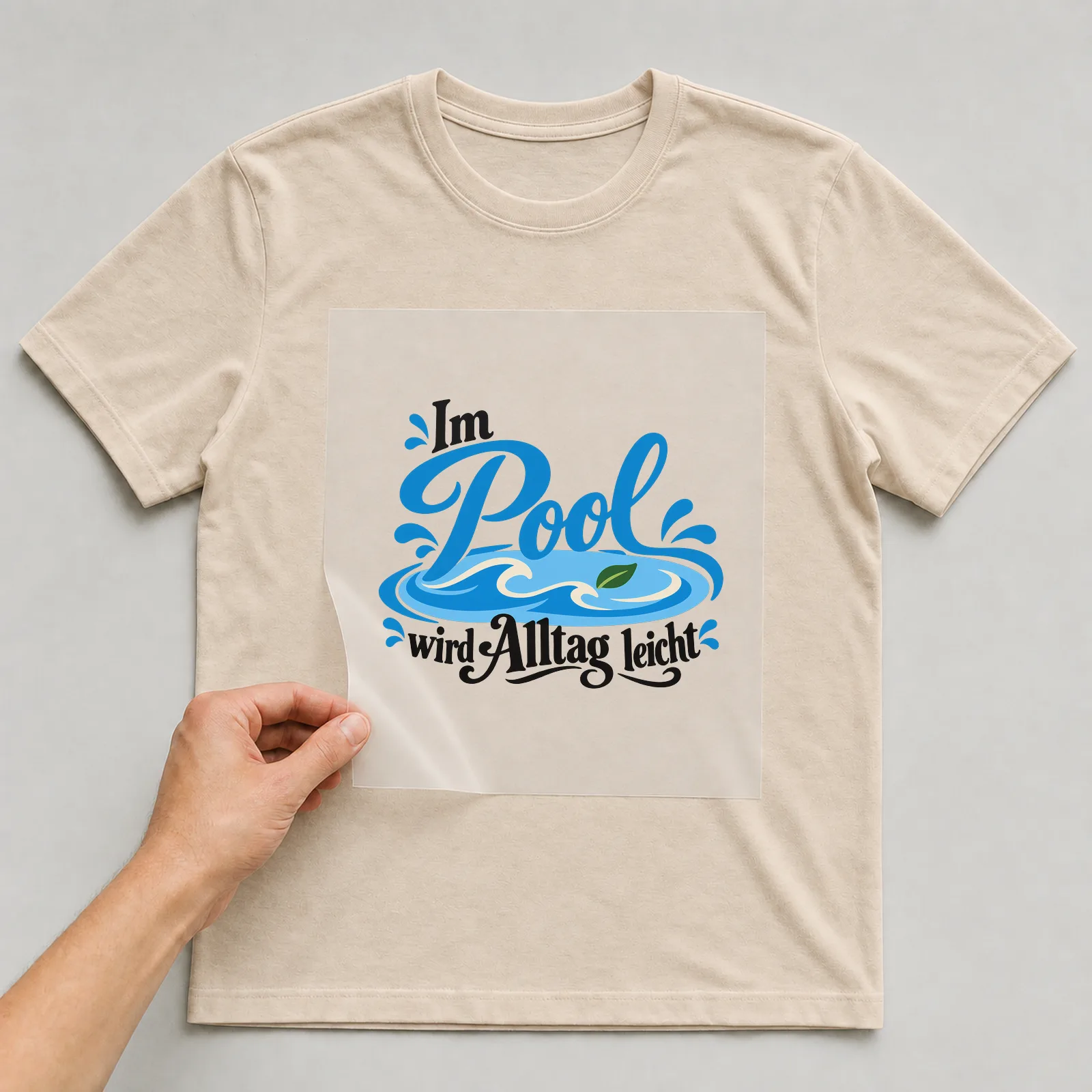 Bügelbild „Im Pool wird Alltag leicht“ auf beigem T-Shirt, Folie wird aufgelegt