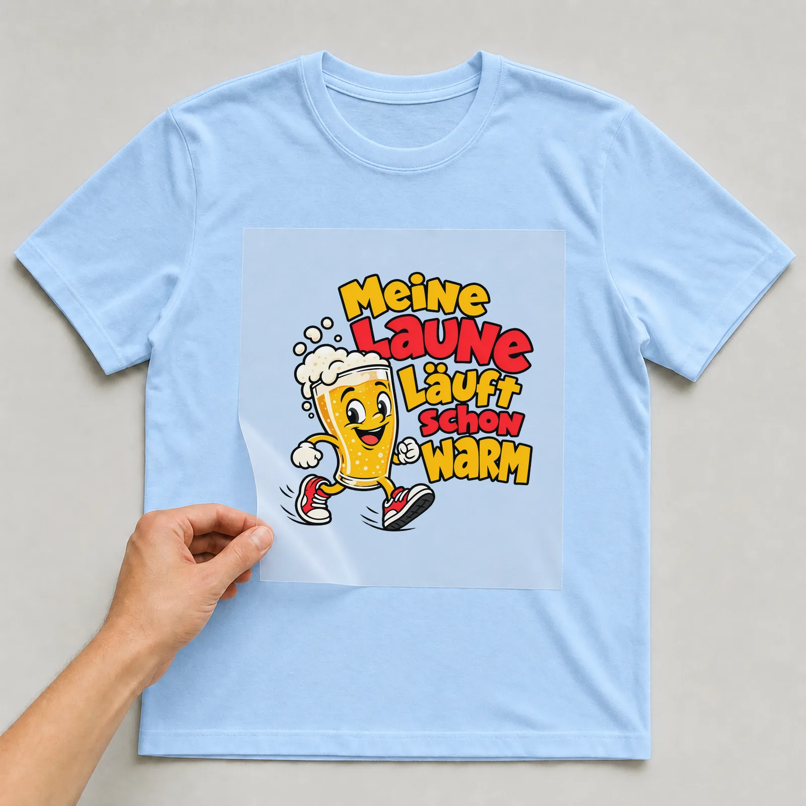 Bügelbild „Meine Laune läuft schon warm“ auf hellblauem T-Shirt, Folie wird aufgelegt