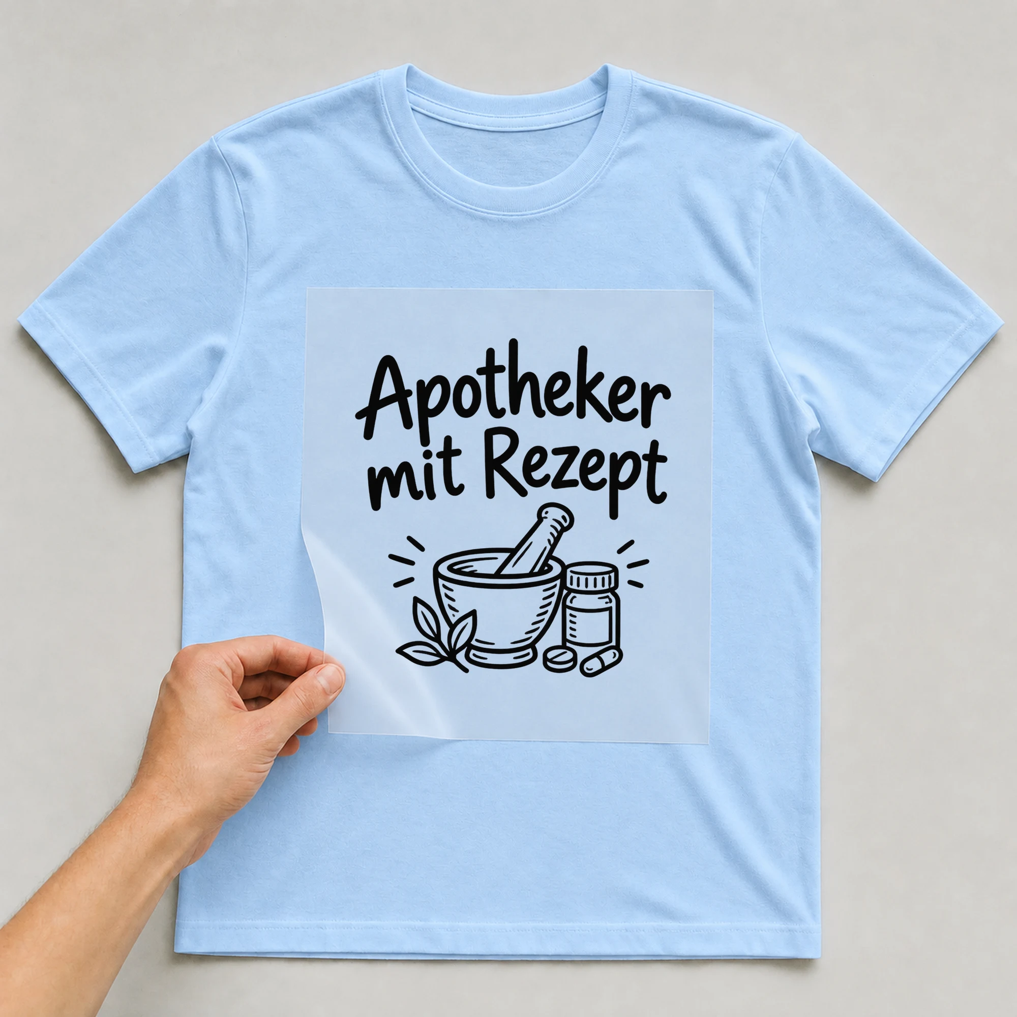 Bügelbild „Apotheker mit Rezept“ auf babyblauem T-Shirt, Folie wird aufgelegt