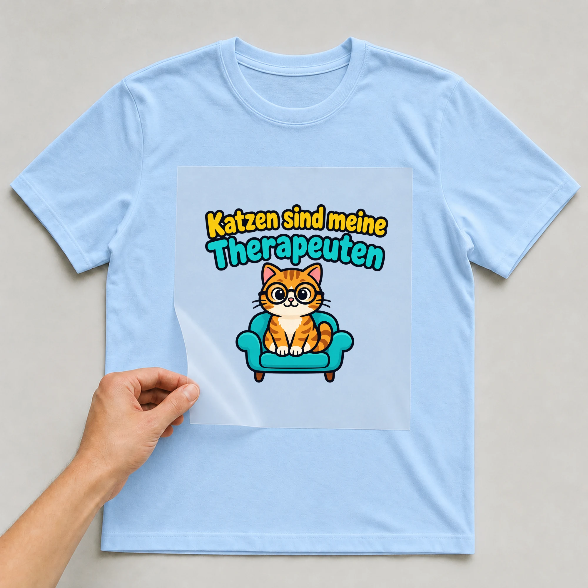 Bügelbild „Katzen sind meine Therapeuten“ auf babyblauem T-Shirt, Folie wird aufgelegt