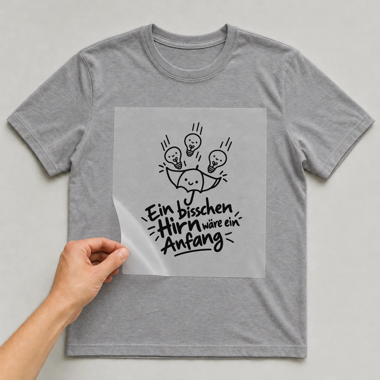 Bügelbild „Ein bisschen Hirn wäre ein Anfang“ auf grauem T-Shirt, Folie wird aufgelegt