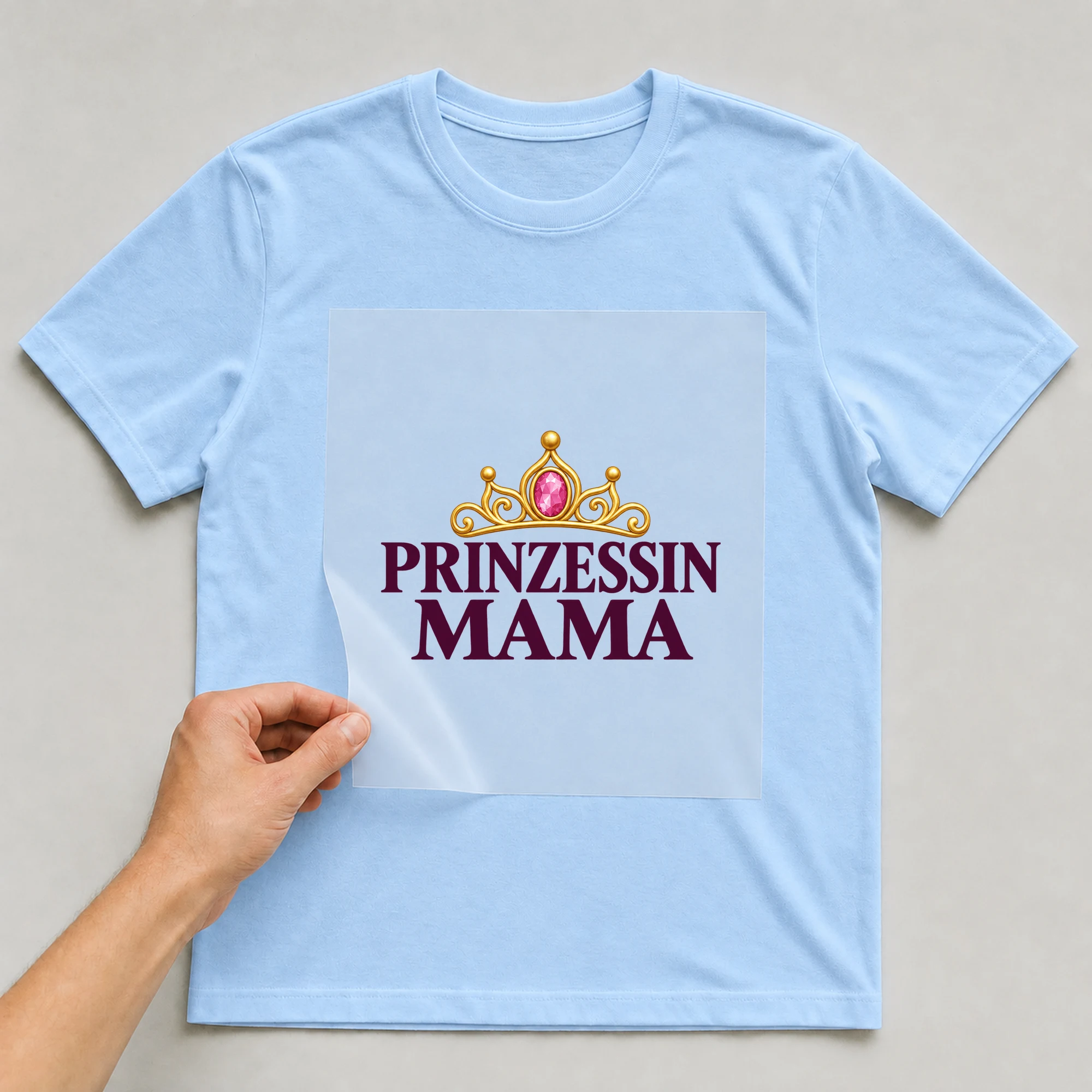 Bügelbild „Prinzessin Mama“ auf babyblauem T-Shirt, Folie wird aufgelegt