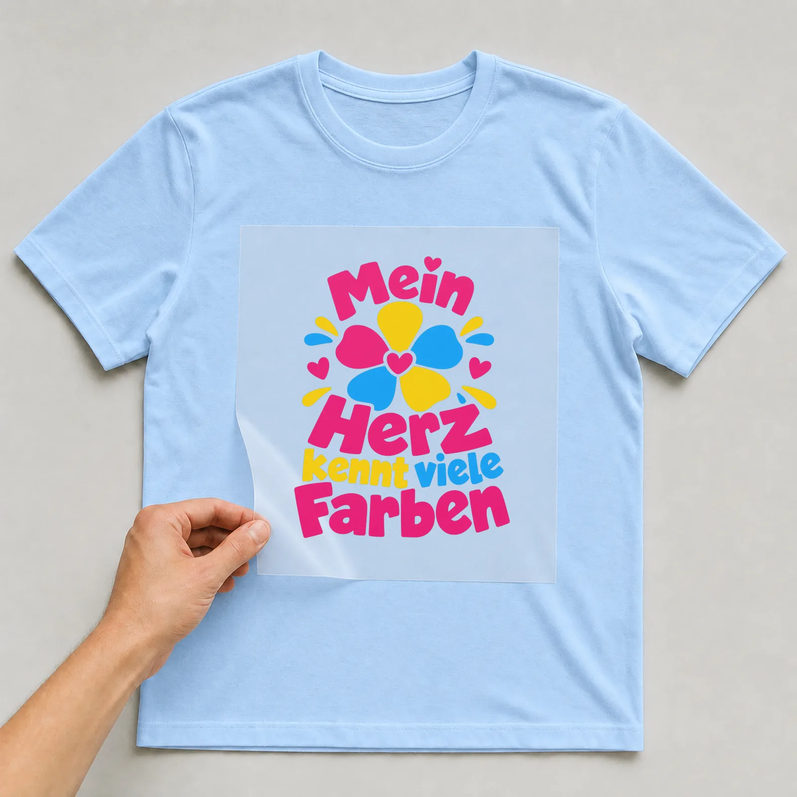 Bügelbild „Mein Herz kennt viele Farben“ auf hellblauem T-Shirt, Folie wird aufgelegt
