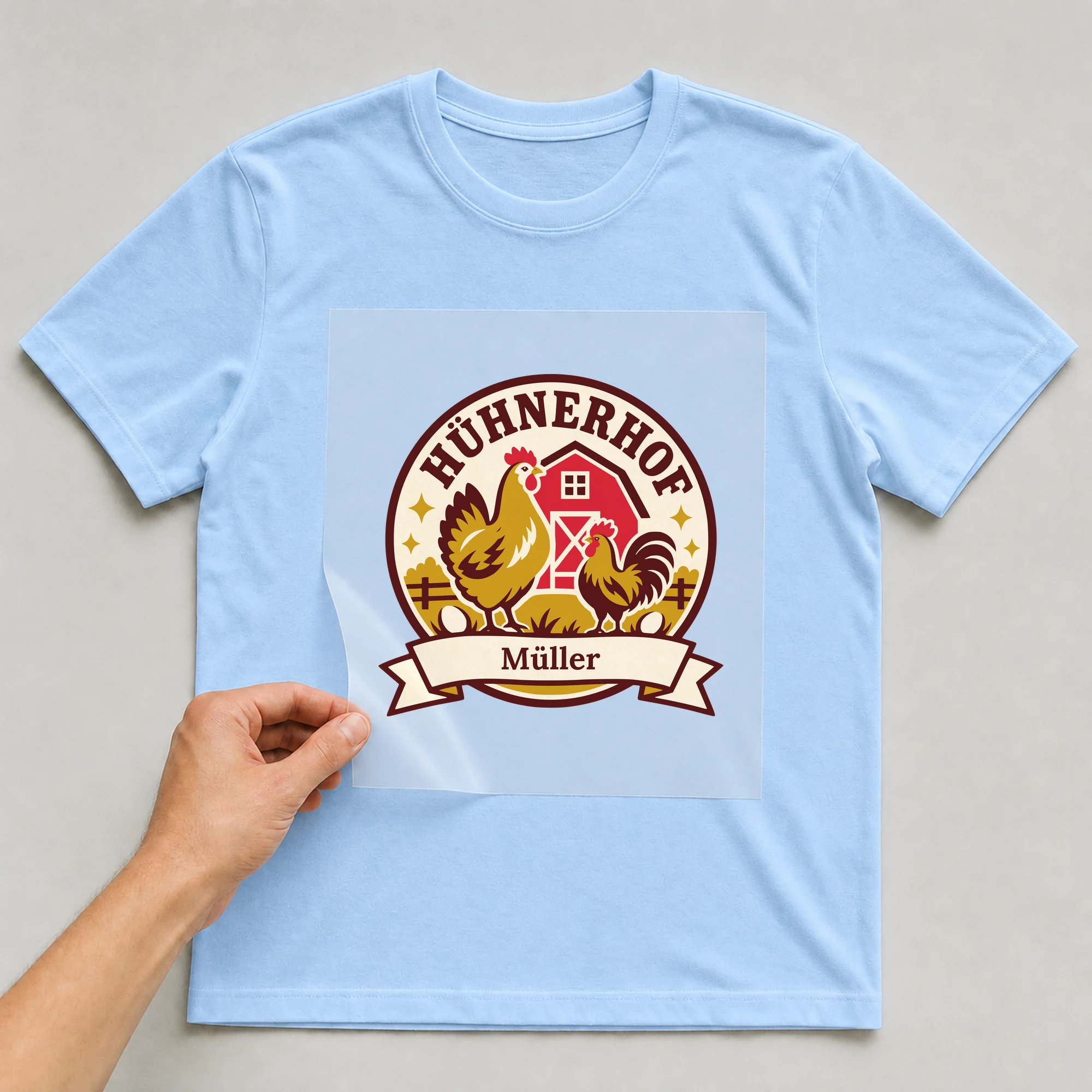 Bügelbild Hühnerhof mit Nachname auf hellblauem T-Shirt, Folie wird aufgelegt