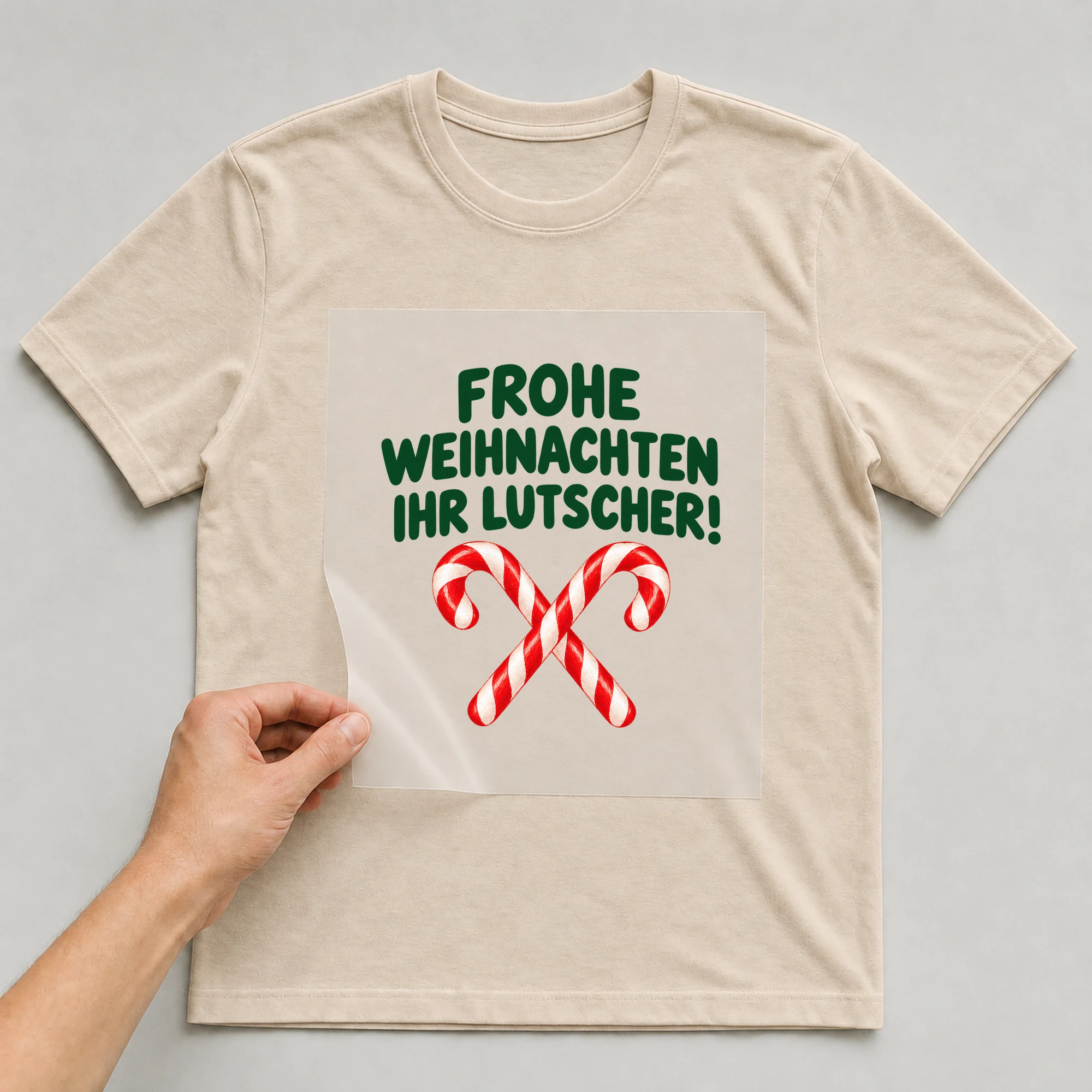 Bügelbild „Frohe Weihnachten ihr Lutscher!“ auf beigem T-Shirt, Folie wird aufgelegt