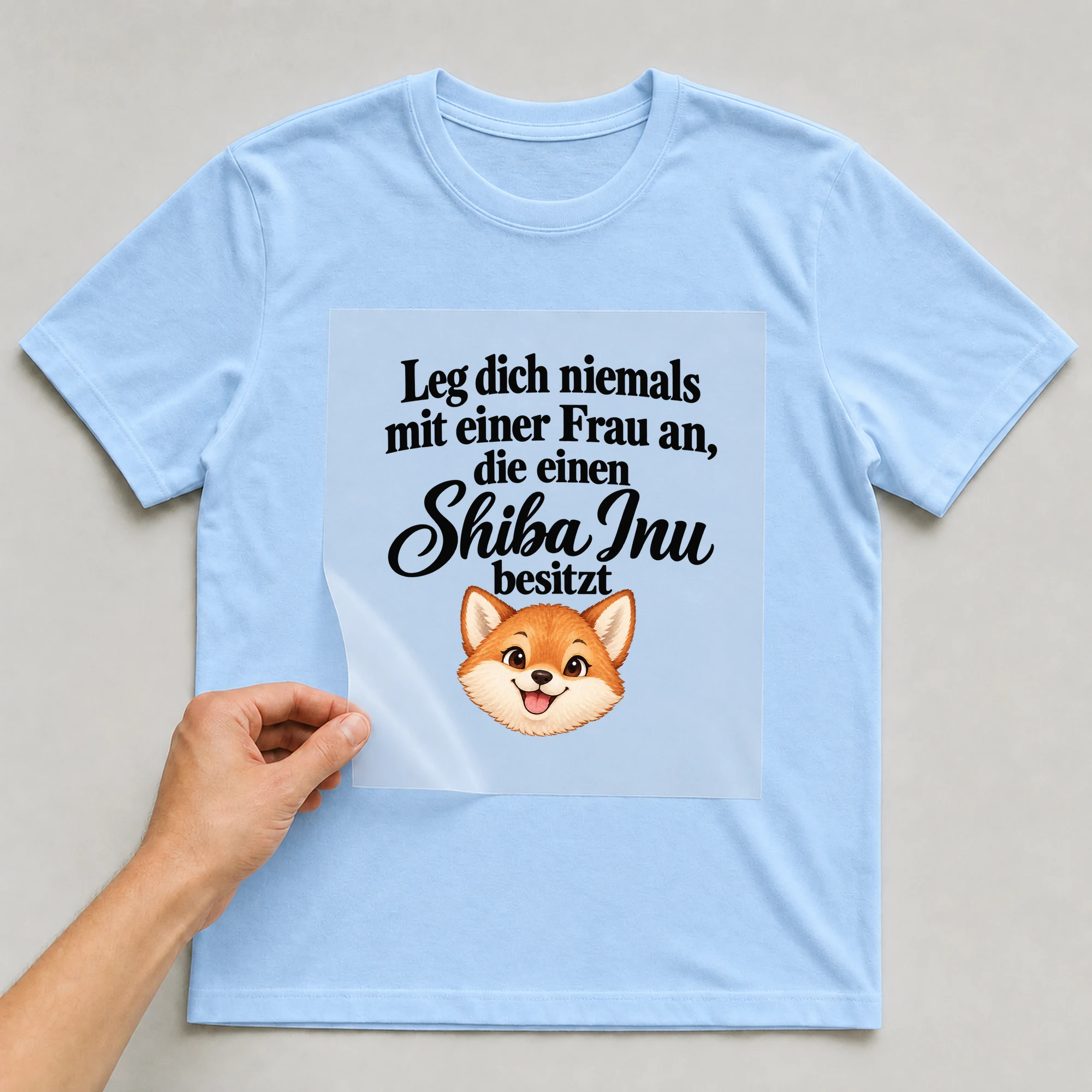 Bügelbild „Leg dich niemals mit einer Frau an, die einen Shiba Inu besitzt“ auf babyblauem T-Shirt, Folie wird aufgelegt