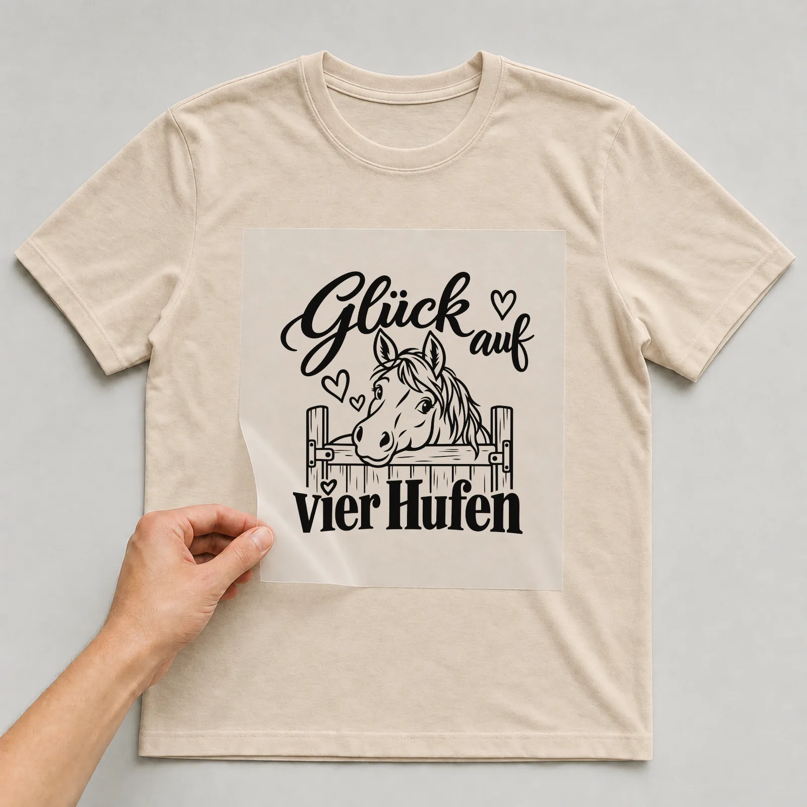 Bügelbild „Glück auf vier Hufen“ auf beigem T-Shirt, Folie wird aufgelegt