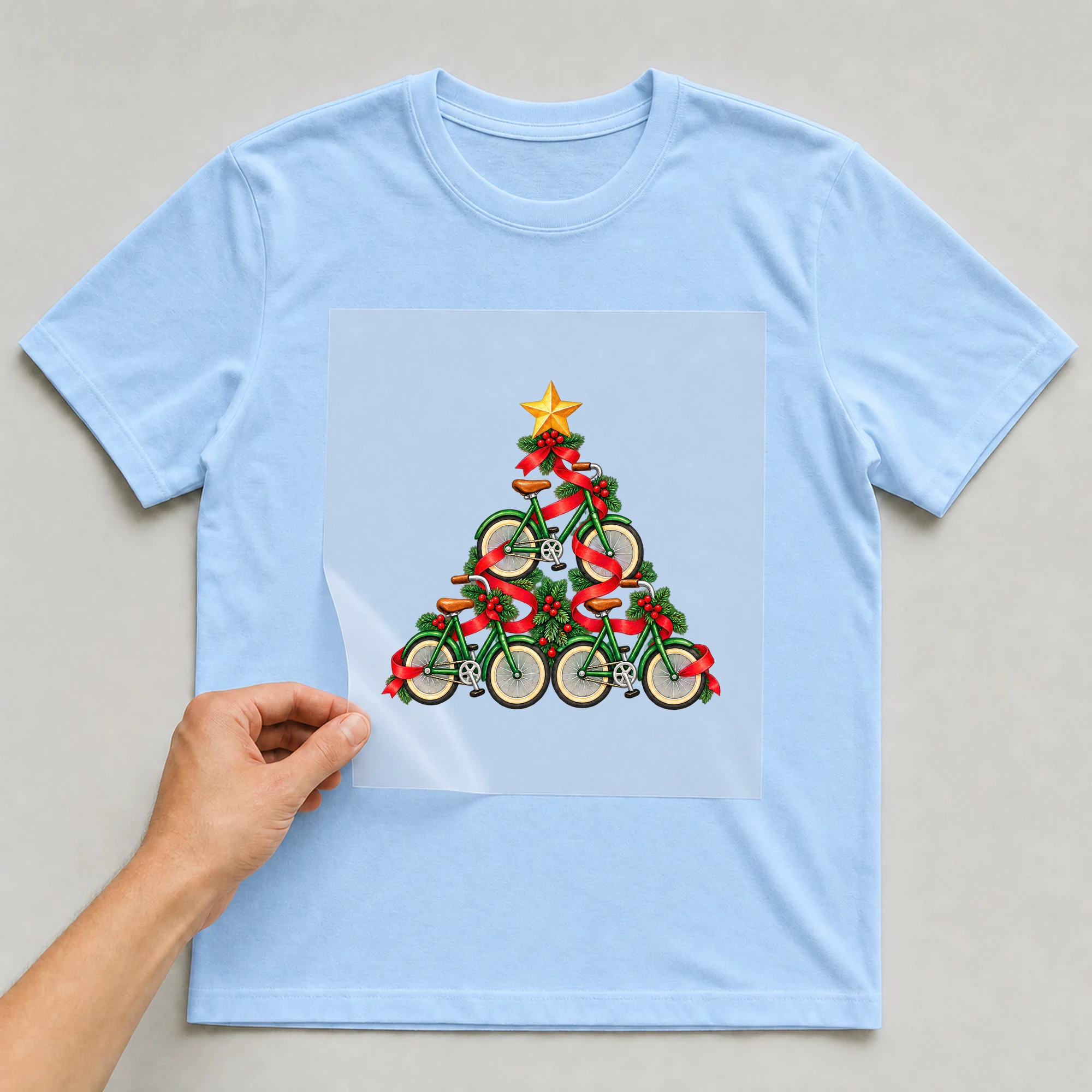 Bügelbild „Weihnachtsbaum aus Fahrrädern“ auf babyblauem T-Shirt, Folie wird aufgelegt