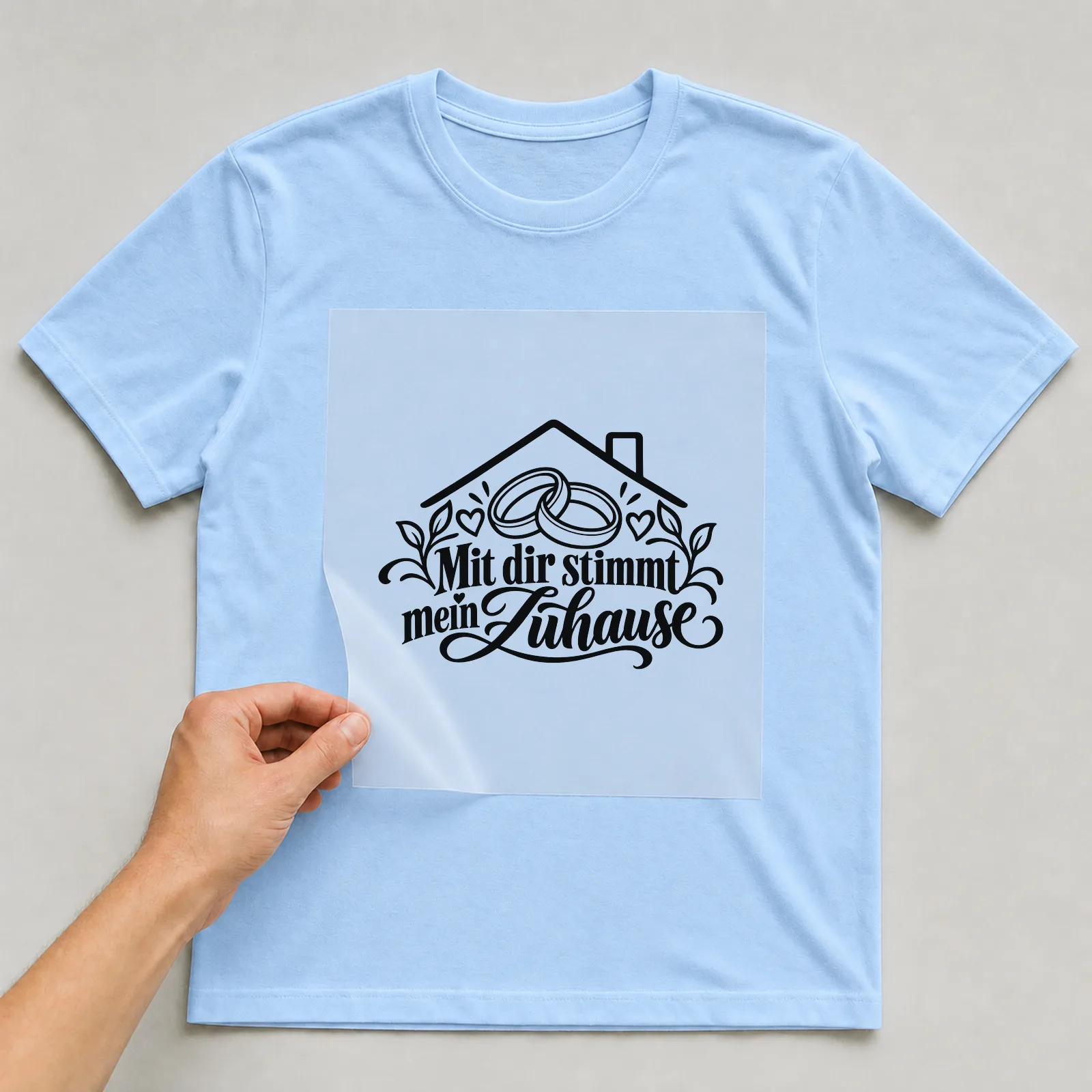 Bügelbild „Mit dir stimmt mein Zuhause“ auf hellblauem T-Shirt, Folie wird aufgelegt