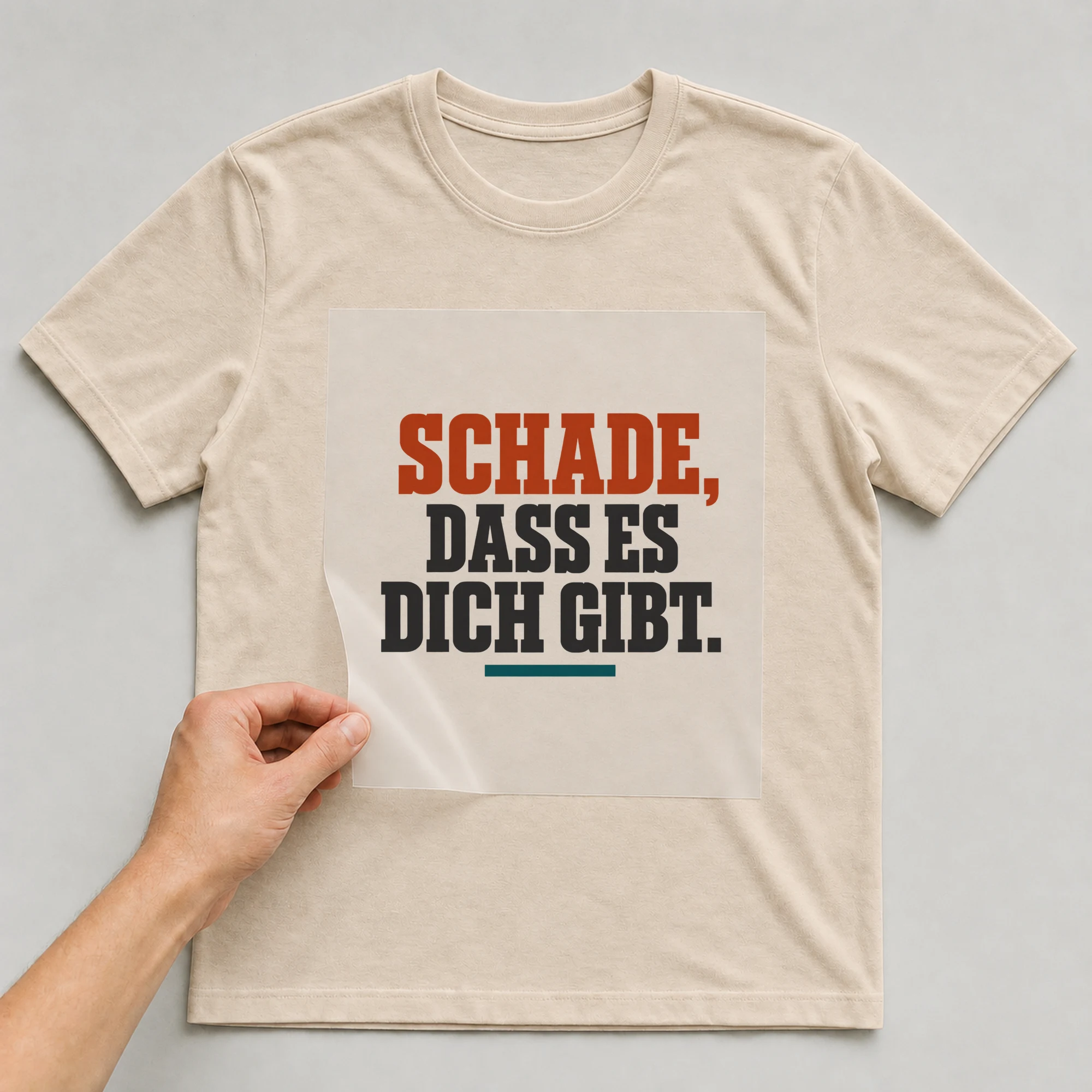 Bügelbild „Schade, dass es dich gibt.“ auf beigem T-Shirt, Folie wird aufgelegt