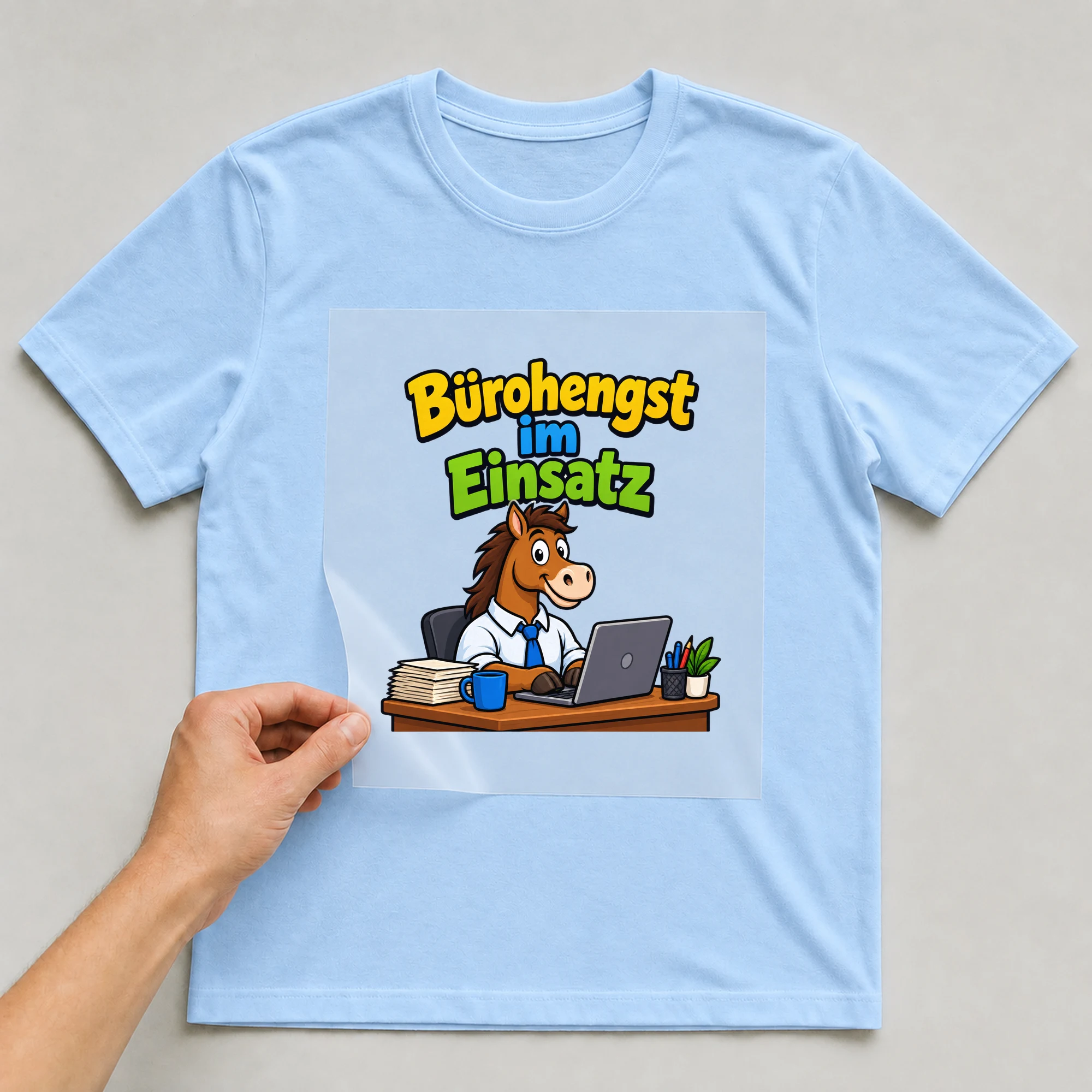 Bügelbild „Bürohengst im Einsatz“ auf babyblauem T-Shirt, Folie wird aufgelegt