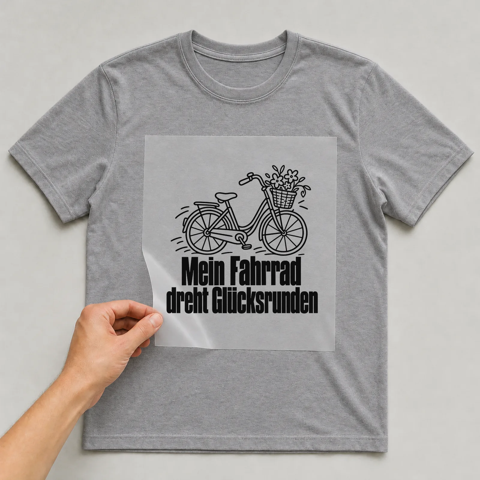Bügelbild „Mein Fahrrad dreht Glücksrunden“ auf grauem T-Shirt, Folie wird aufgelegt